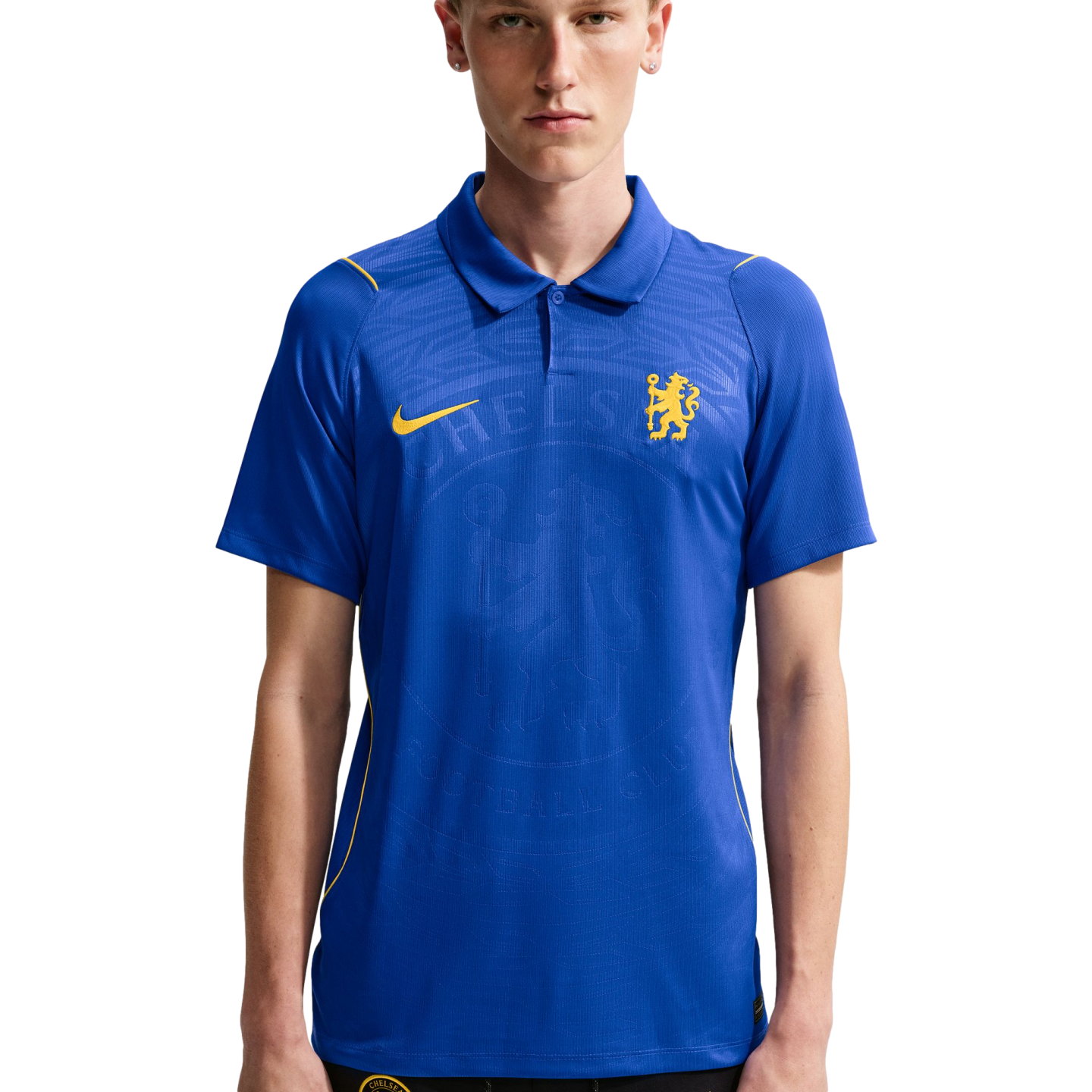 A young man wearing a blue Nike Chelsea FC polo shirt with yellow accents and an embossed club crest, set against a plain white background.