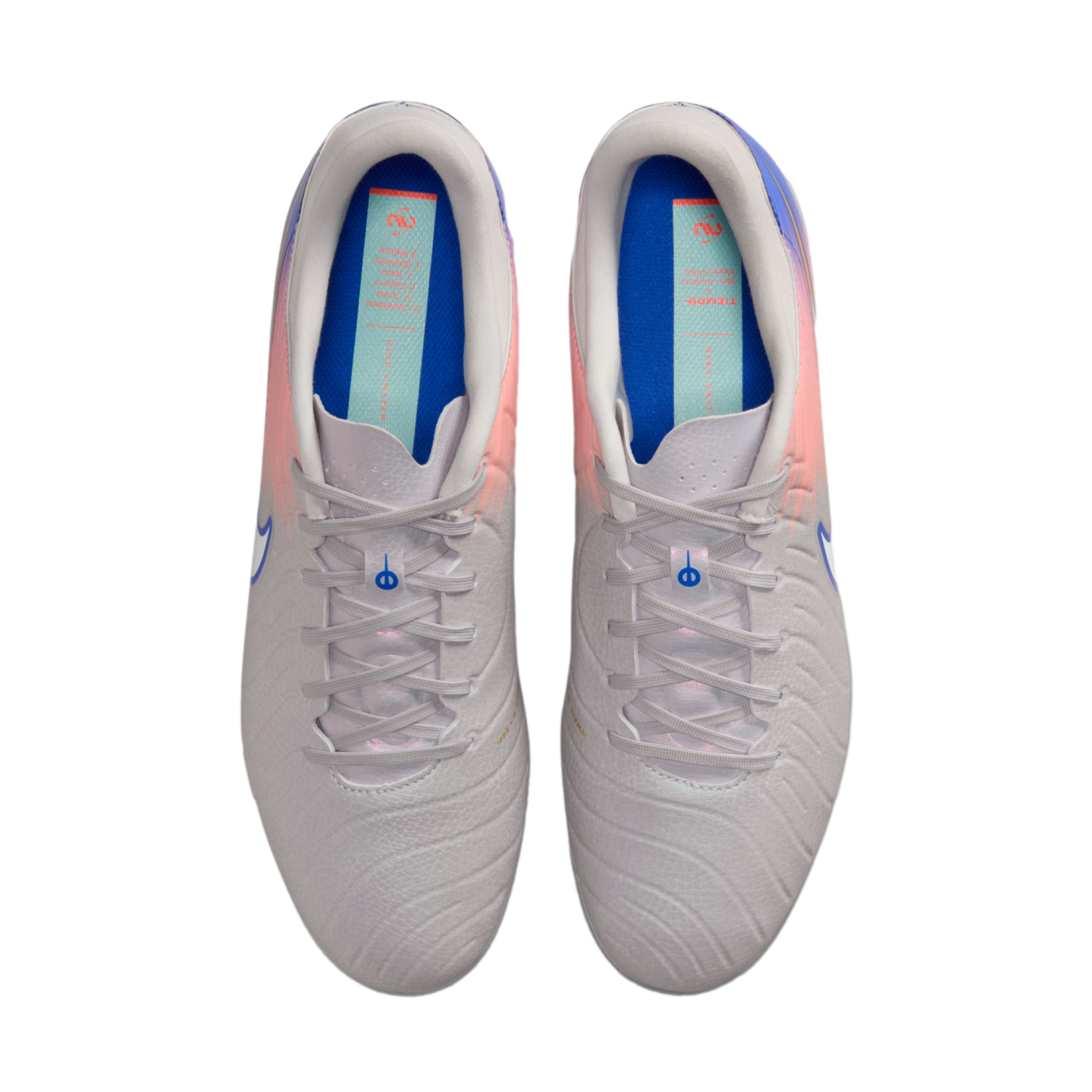Top-down view of a pair of light grey Nike soccer cleats with pink and purple accents and blue insoles, centered against a solid black background.