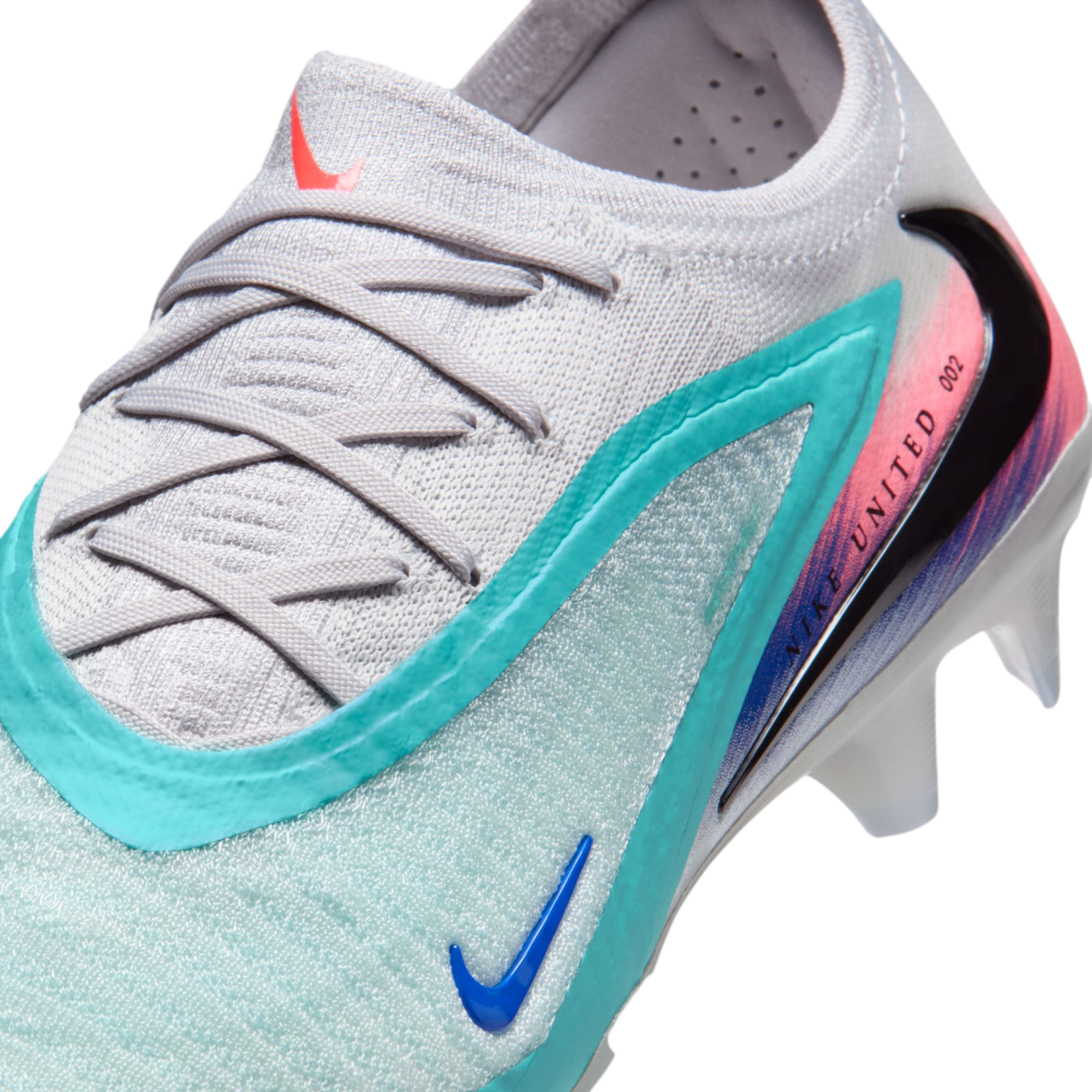A close-up of a light gray Nike soccer cleat with teal, pink, and blue accents, featuring the text "NIKE UNITED 002" and a black swoosh.