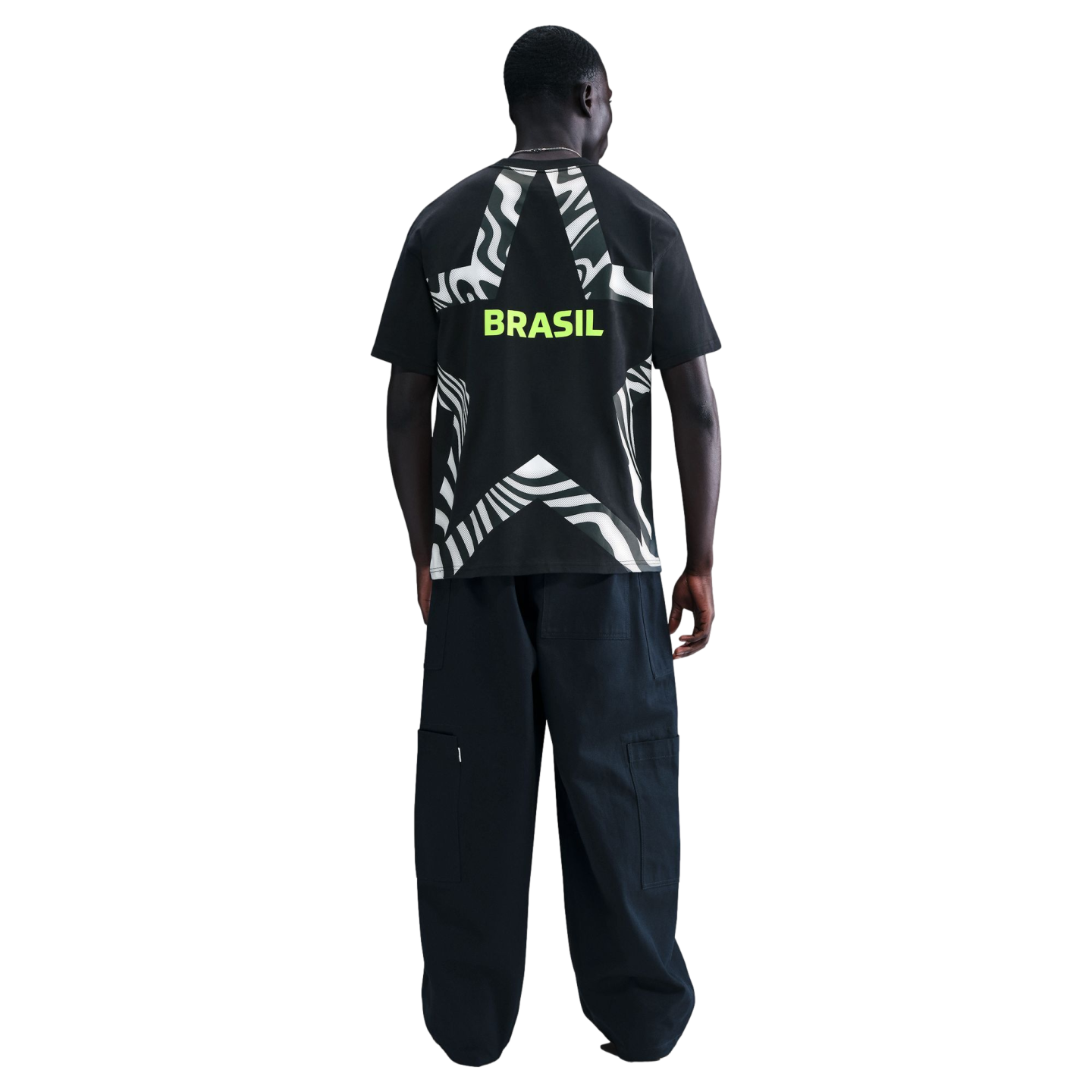 Back view of a man wearing a black t-shirt with a large graphic star and "BRASIL" in lime green, paired with dark baggy cargo pants.