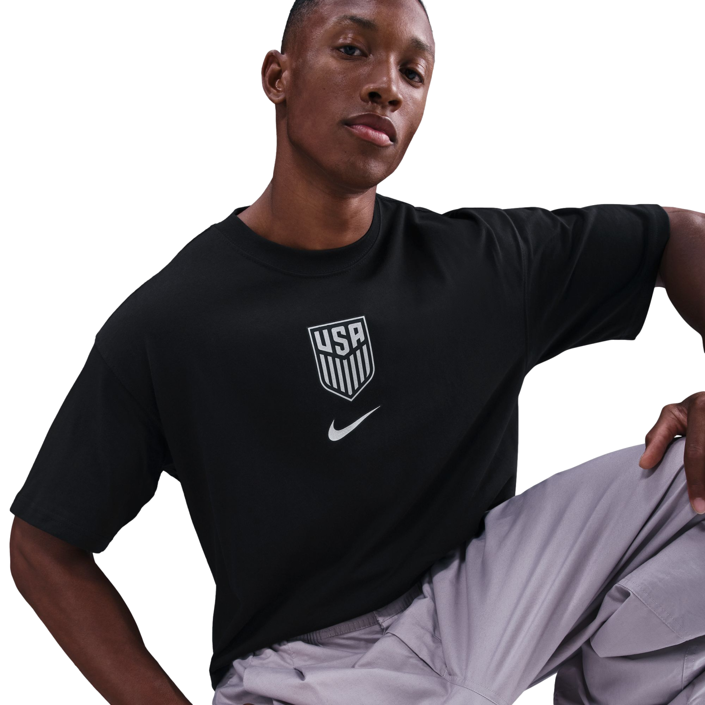A man wearing a black Nike USA soccer T-shirt and grey cargo pants poses against a black background.