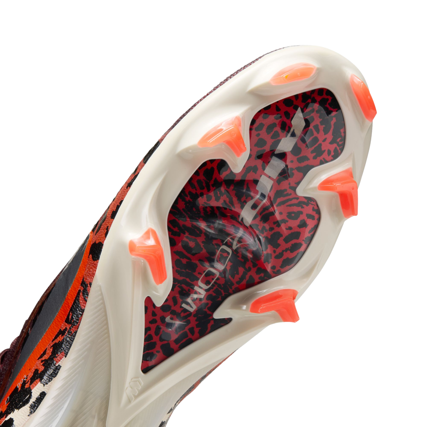 A close-up, angled view of the sole of a Nike soccer cleat. It features a cream-colored soleplate with bright orange bladed studs and a central red and black animal-print panel with "AIR ZOOM" written in silver.