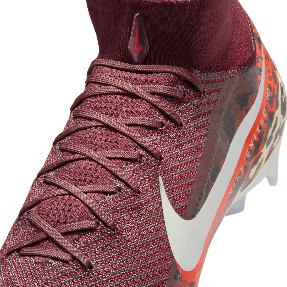 A close-up, high-angle shot shows a maroon Nike soccer cleat against a black background. The shoe features a textured, knit upper with maroon laces and a high-top sock collar. A small, teardrop-shaped logo with a red swoosh is on the front of the collar,