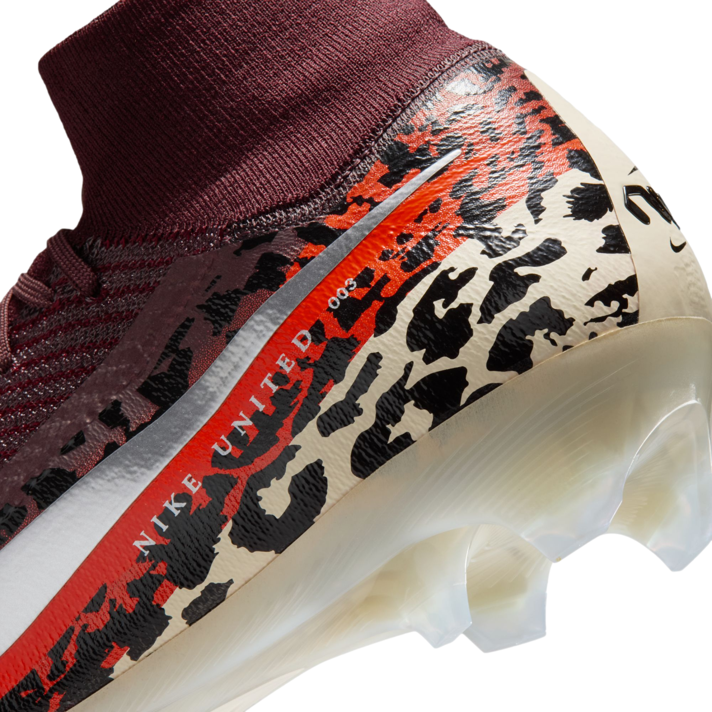 A close-up, angled view of the heel and ankle area of a Nike soccer cleat against a black background. The shoe features a burgundy ribbed knit ankle collar and a main body decorated with a bold leopard-print pattern in cream, black, and vibrant orange. A