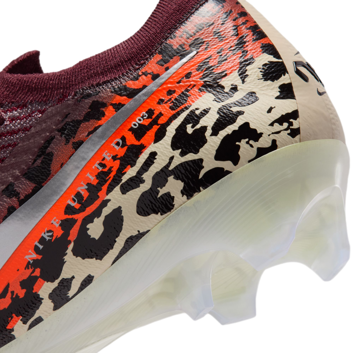 A close-up view of the heel of a Nike soccer cleat featuring a vibrant leopard print in black, orange, and beige. The text "NIKE UNITED 003" is visible along a silver stripe, and the shoe has a translucent white soleplate with clear studs.