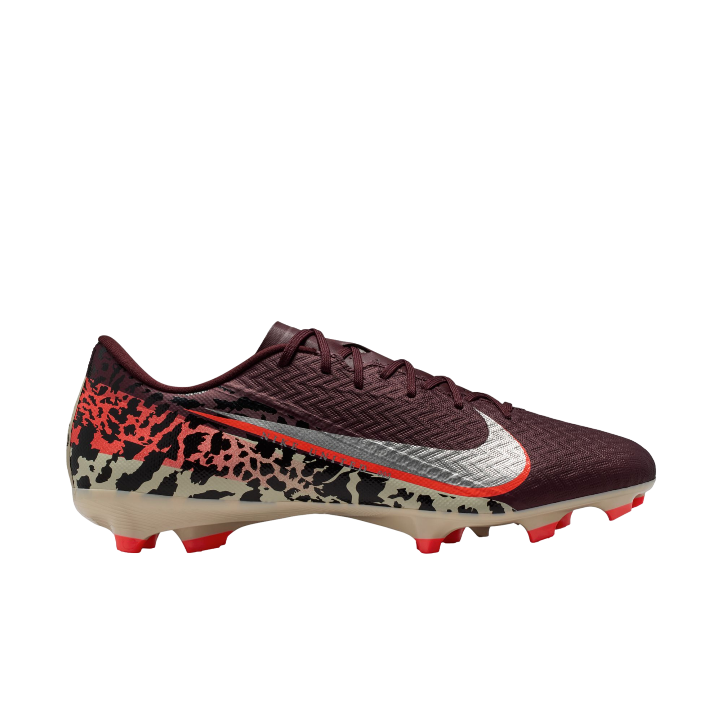 A profile view of a Nike soccer cleat against a solid black background. The shoe features a textured maroon upper, a large silver Nike Swoosh with an orange border, and a bold abstract graphic pattern in tan, black, and orange across the lower half and he
