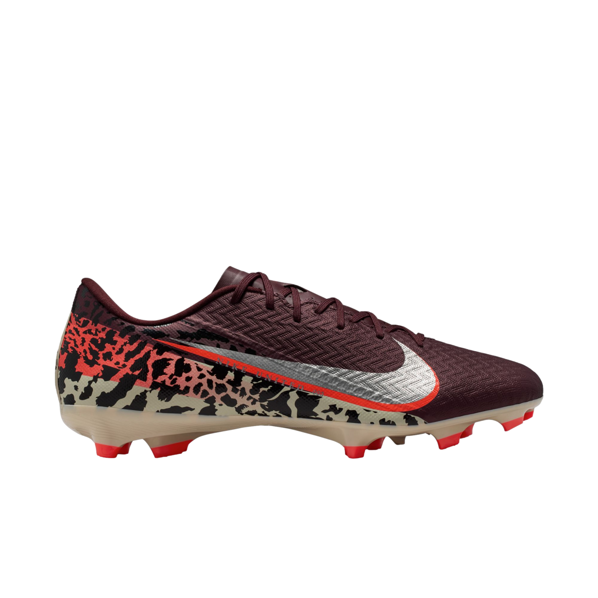 A profile view of a Nike soccer cleat against a solid black background. The shoe features a textured maroon upper, a large silver Nike Swoosh with an orange border, and a bold abstract graphic pattern in tan, black, and orange across the lower half and he
