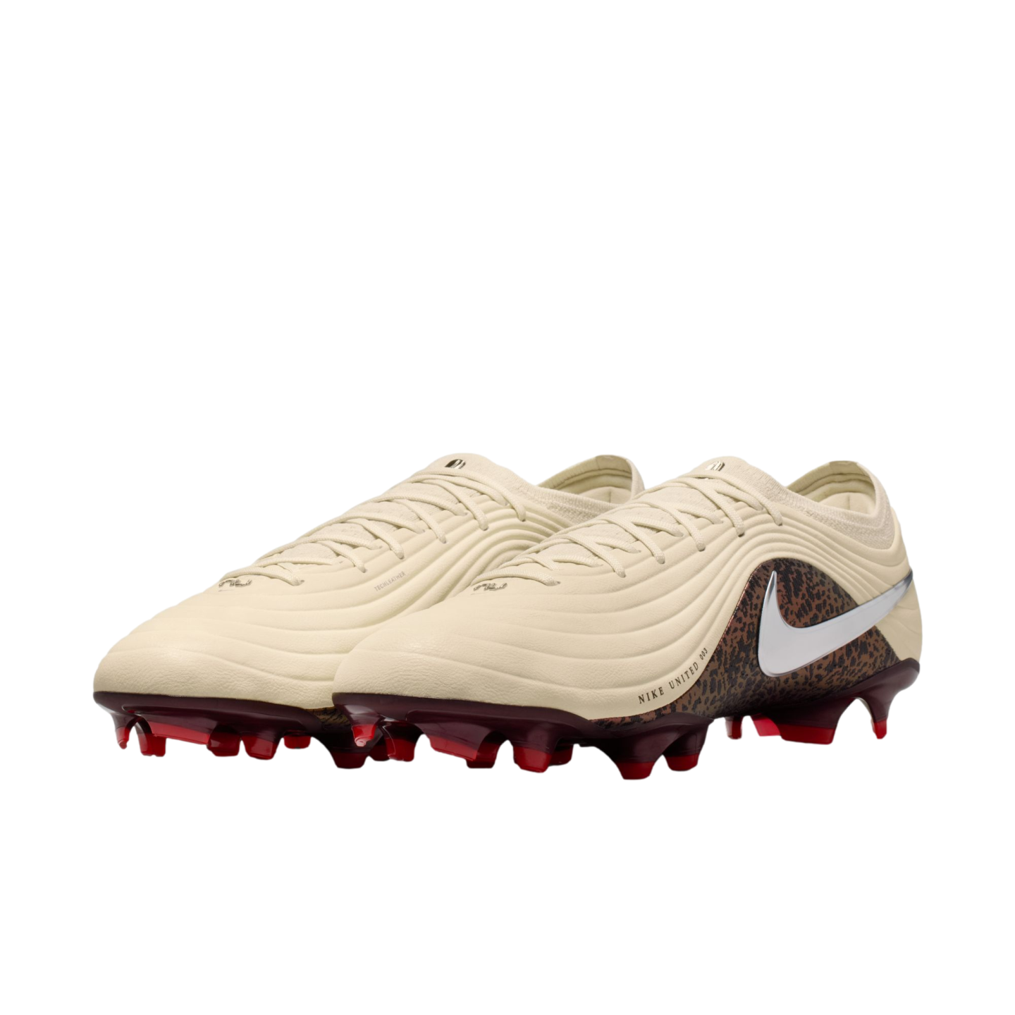 A pair of cream-colored Nike soccer cleats with a textured upper, animal-print heel, silver swoosh logo, and dark red studs against a black background.