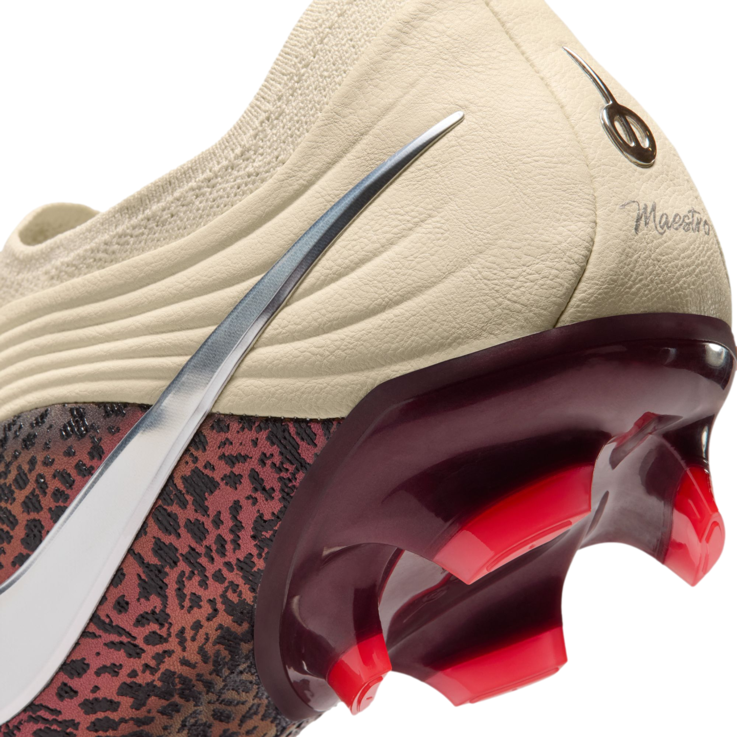 A close-up view of the heel and soleplate of a Nike soccer cleat against a black background. The upper features a cream-colored textured heel with a script "Maestro" inscription and a silver metallic Nike Swoosh. A glossy, deep-red translucent heel counte