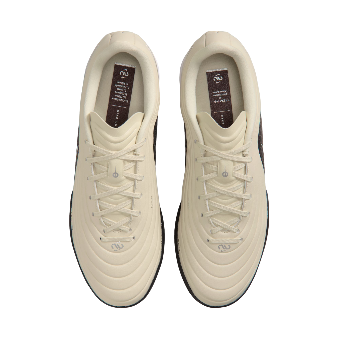 Top-down view of a pair of cream-colored Nike Tiempo soccer cleats with textured uppers and matching laces, set against a solid black background.