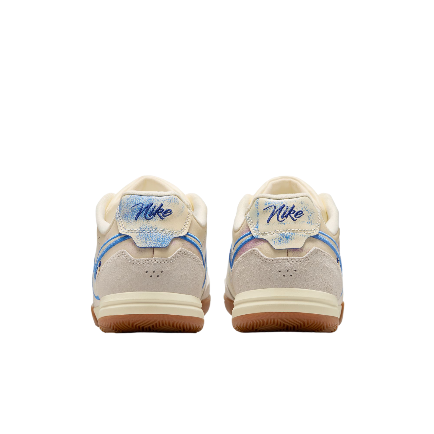 A rear view of a pair of Nike sneakers featuring cream and light gray suede uppers, script Nike logos on distressed blue heel tabs, and gum rubber outsoles against a solid black background.