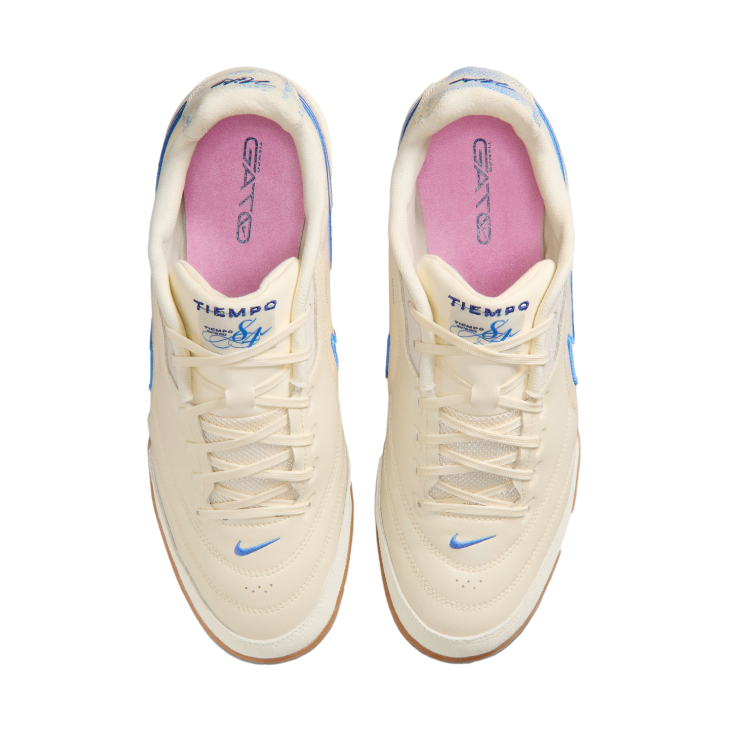 Top-down view of a pair of off-white Nike Tiempo Gato sneakers with light blue accents, pink insoles, and gum rubber outsoles, set against a solid black background.