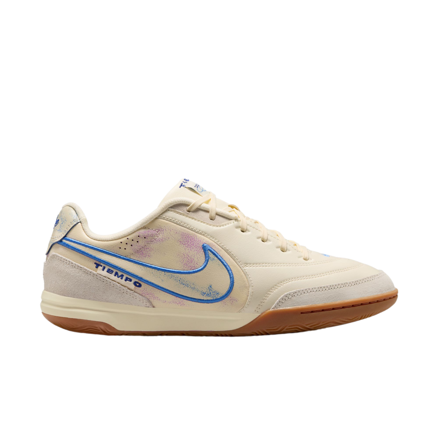 A profile view of a cream-colored Nike Tiempo indoor soccer shoe against a solid black background. The shoe features a blue-outlined Nike swoosh with a faded purple and blue interior, light grey suede overlays on the toe and heel, and a brown gum rubber o