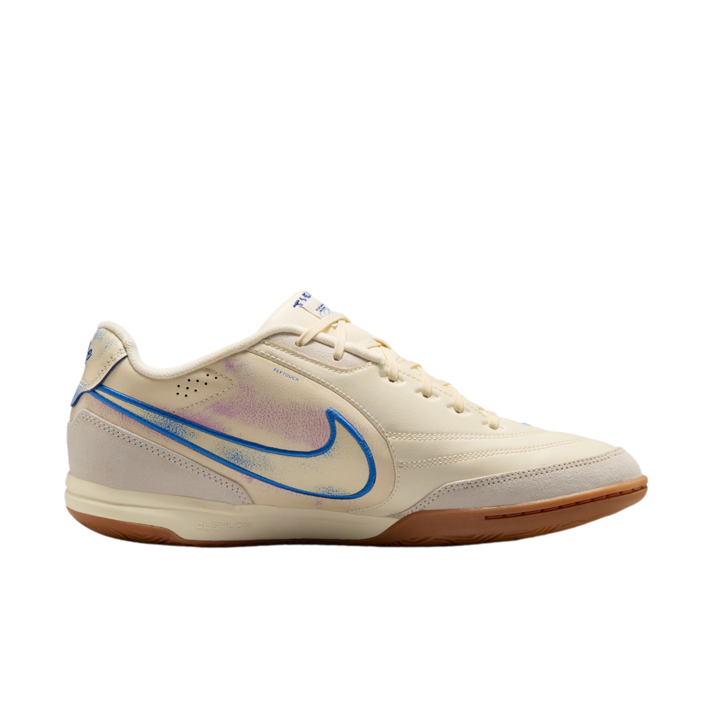 A side profile of a cream-colored Nike indoor soccer shoe against a black background, featuring a blue swoosh with purple accents and a brown gum sole.