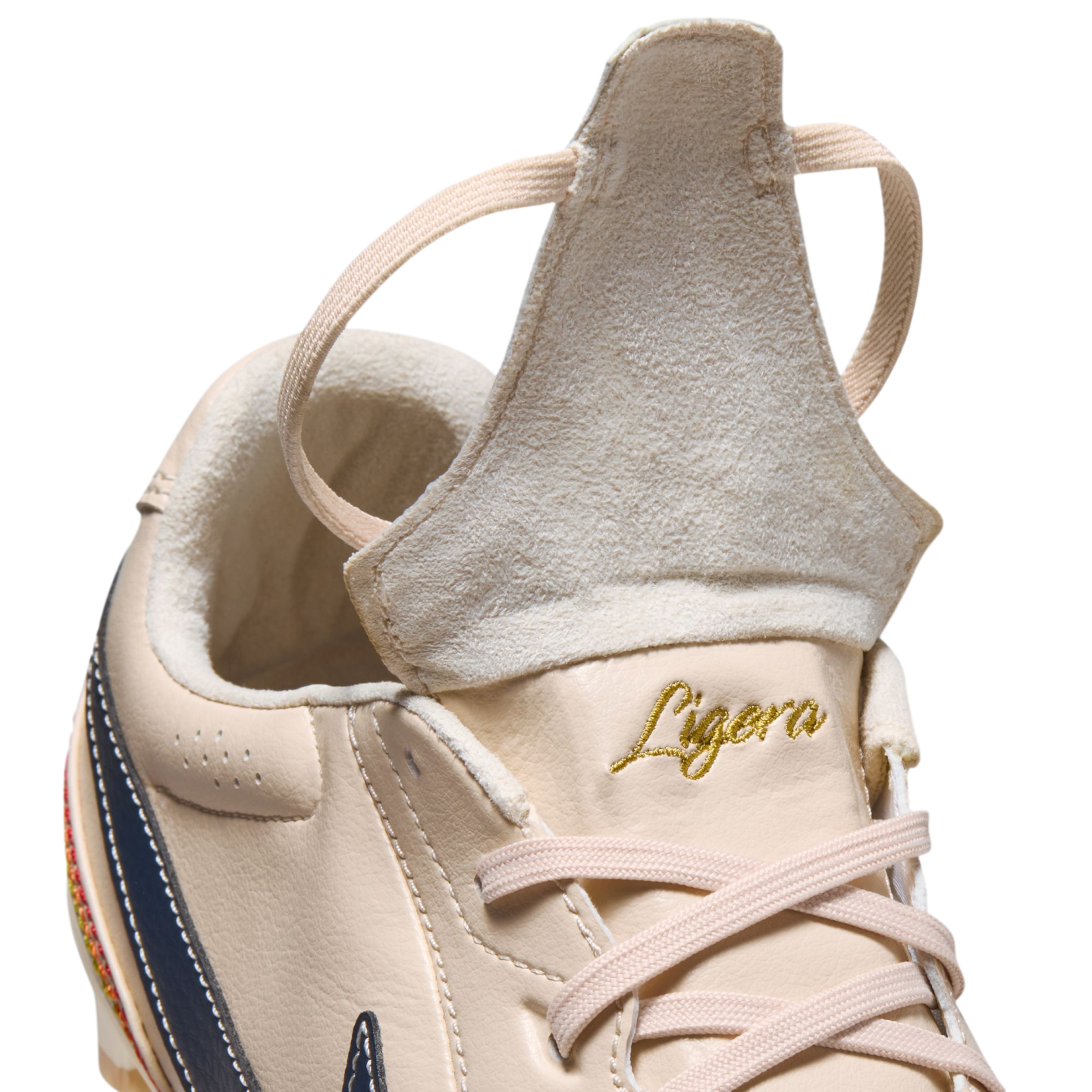 A close-up of a beige leather athletic shoe with its tongue flipped up. The word "Ligera" is embroidered in gold script above beige laces.