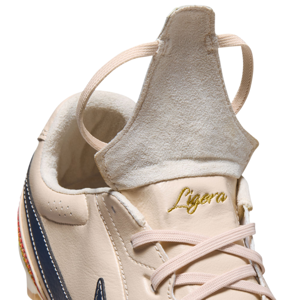 A close-up of a beige leather athletic shoe with its tongue flipped up. The word "Ligera" is embroidered in gold script above beige laces.