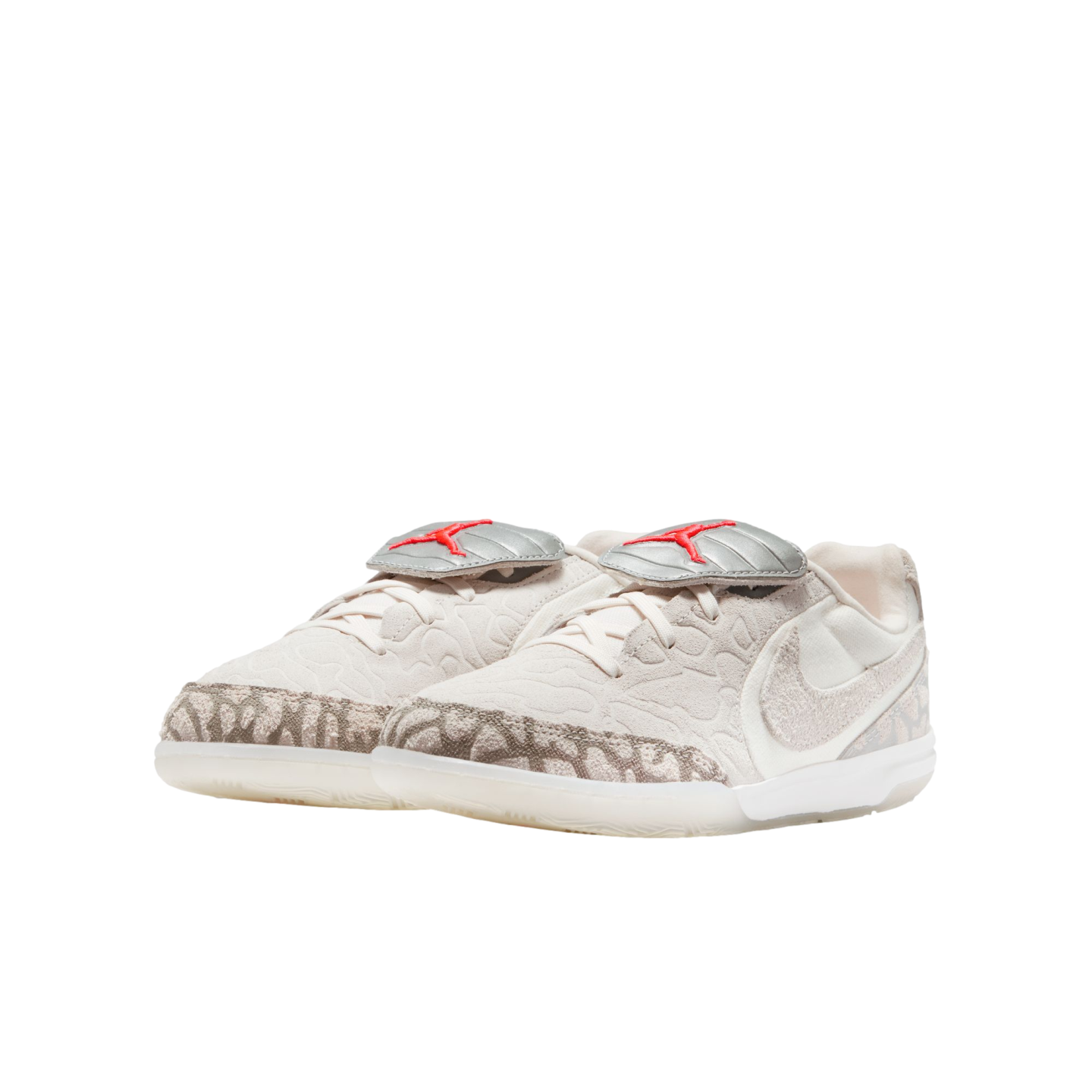 Beige low-top Jordan sneakers with textured uppers, patterned mudguards, and silver lace shrouds featuring red Jumpman logos, shown against a black background.