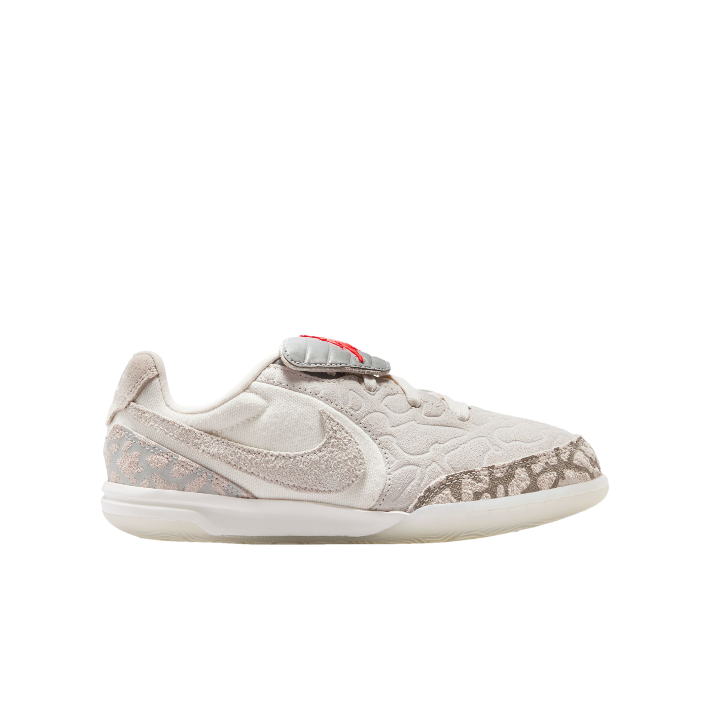 Side profile of a pale grey and cream low-top Nike shoe featuring a textured upper, fuzzy swoosh, and a red tongue accent on a black background.