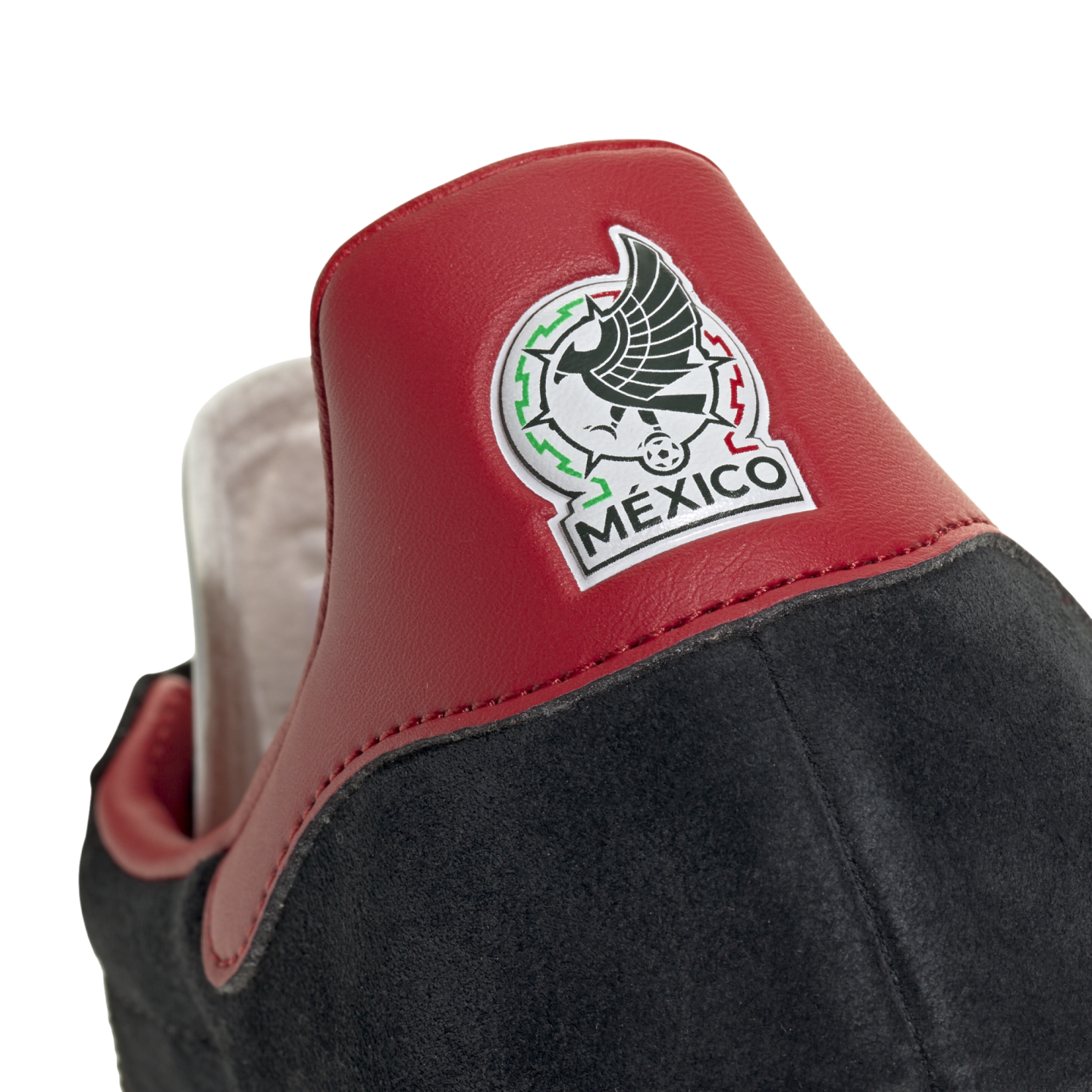 Close-up of the heel of a black suede shoe with a red leather tab featuring the embroidered Mexico national football team logo.