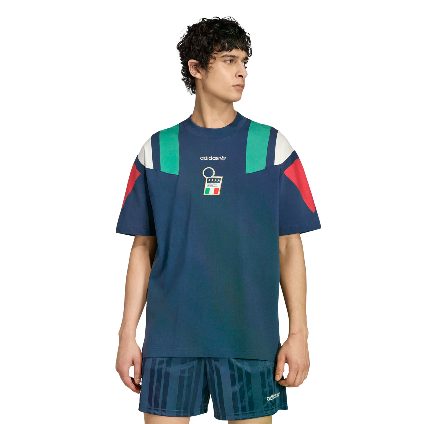 A man wearing a navy blue Adidas t-shirt with teal and red color-blocked shoulders and an Italian crest, paired with matching striped shorts.