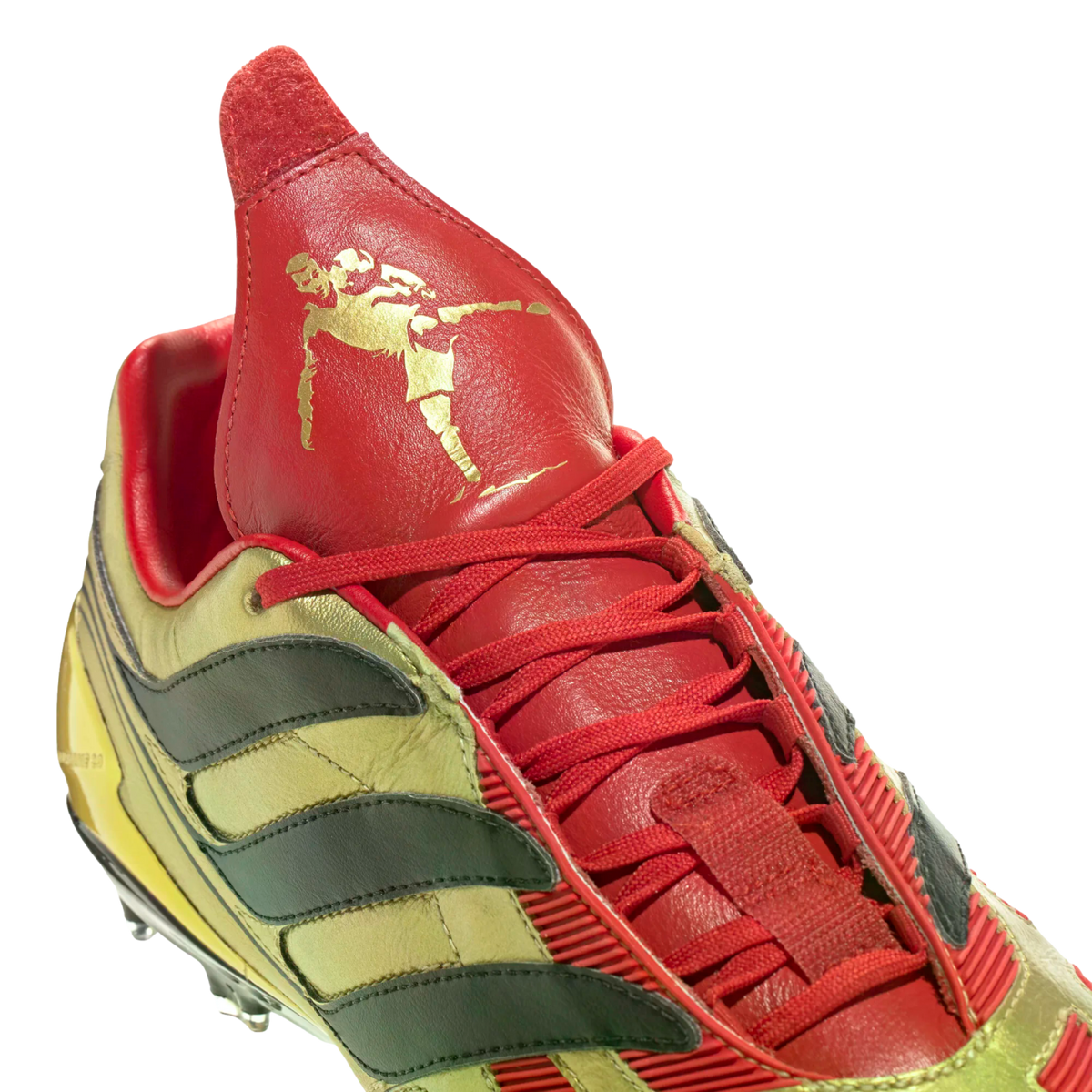 Close-up of a red and gold Adidas Predator soccer cleat. It features a prominent red fold-over tongue with a gold silhouette of David Beckham.