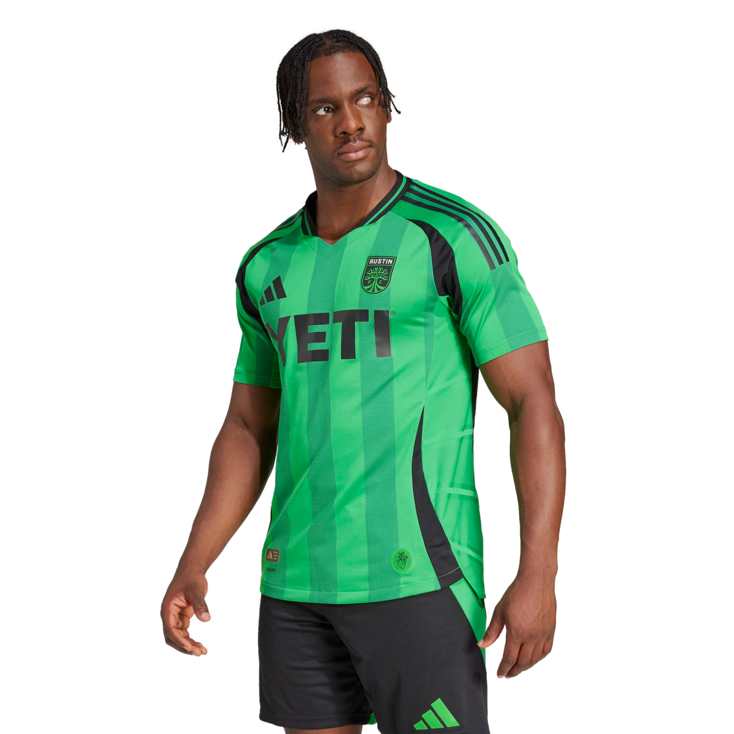 A man models a green Austin FC soccer jersey with a black YETI sponsor logo and black shorts against a white background.