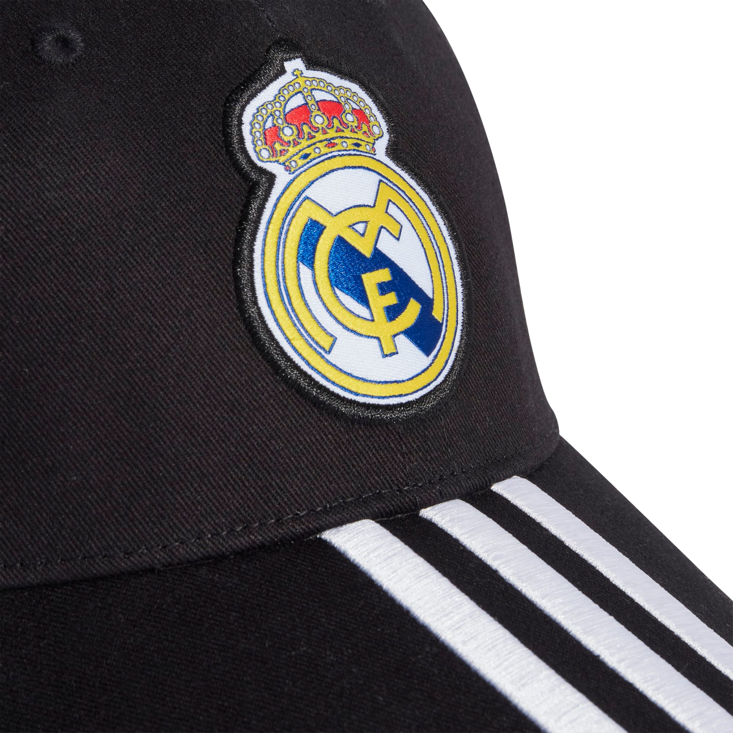 Close-up of a black baseball cap featuring the Real Madrid crest and three white stripes on the brim.