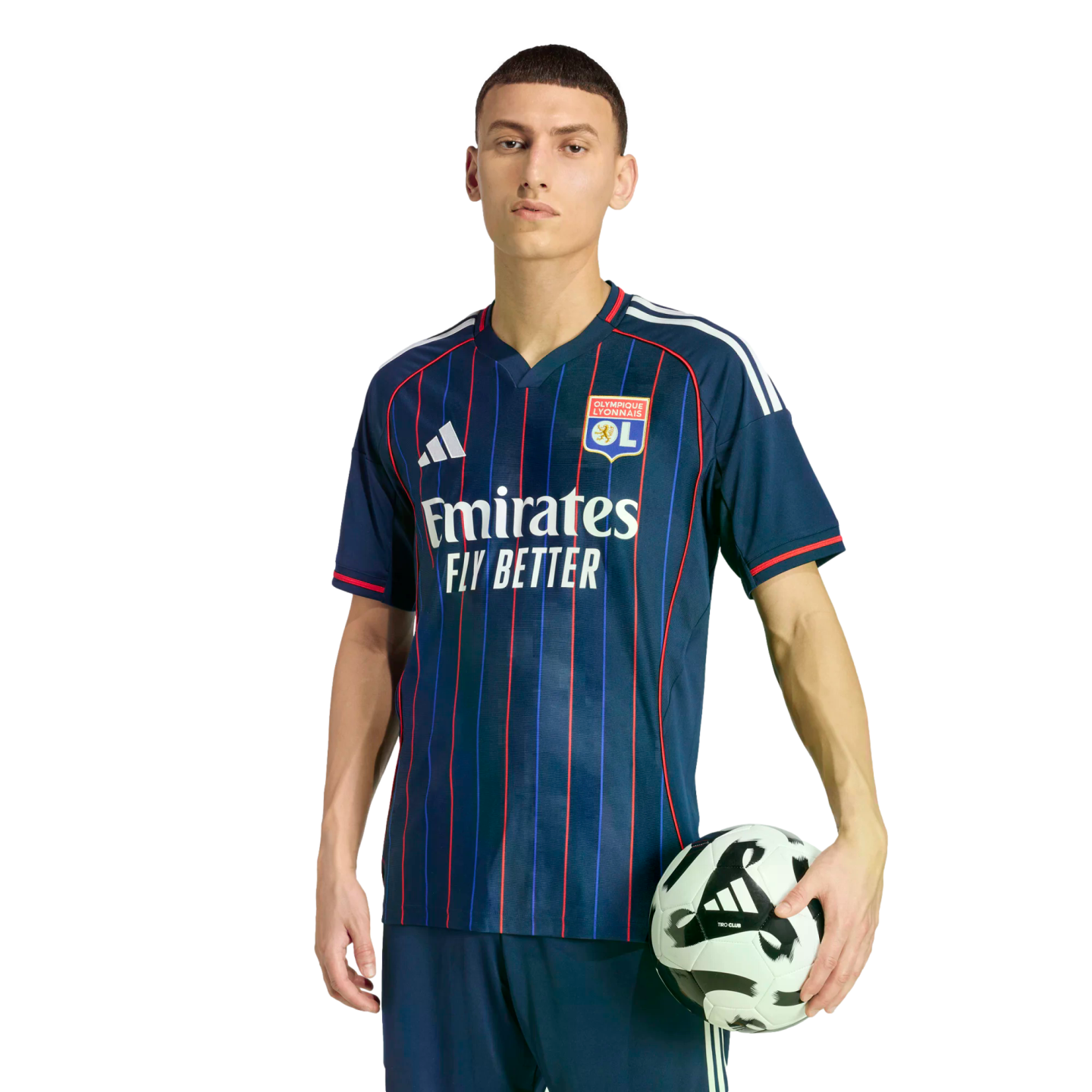 A man in a navy Olympique Lyonnais soccer kit with red and blue stripes, holding a soccer ball against a black background.