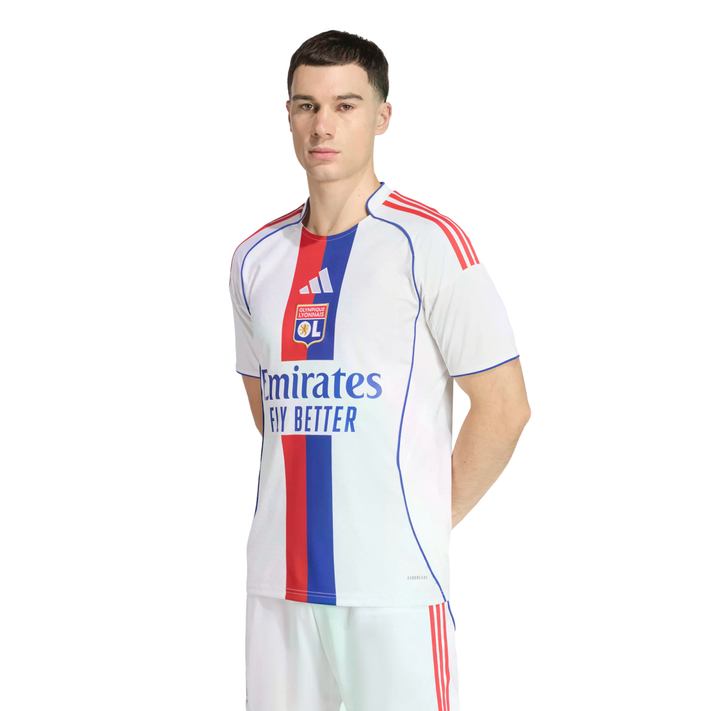 A man models the white Olympique Lyonnais home soccer jersey featuring a central red and blue stripe, team crest, and Emirates sponsor. He stands against a solid black background.