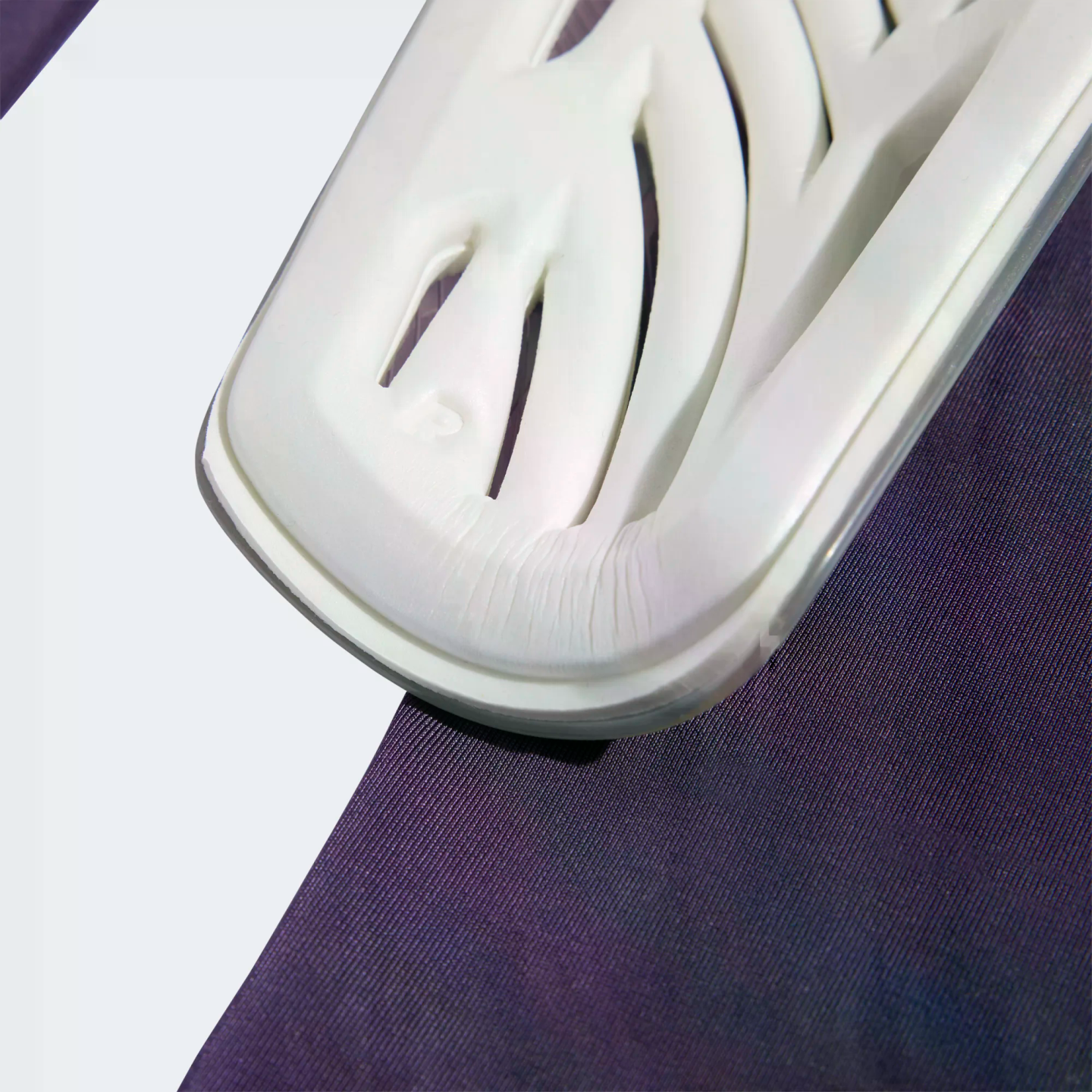 Close-up of a white textured sports shin guard with cutouts, resting on purple fabric.