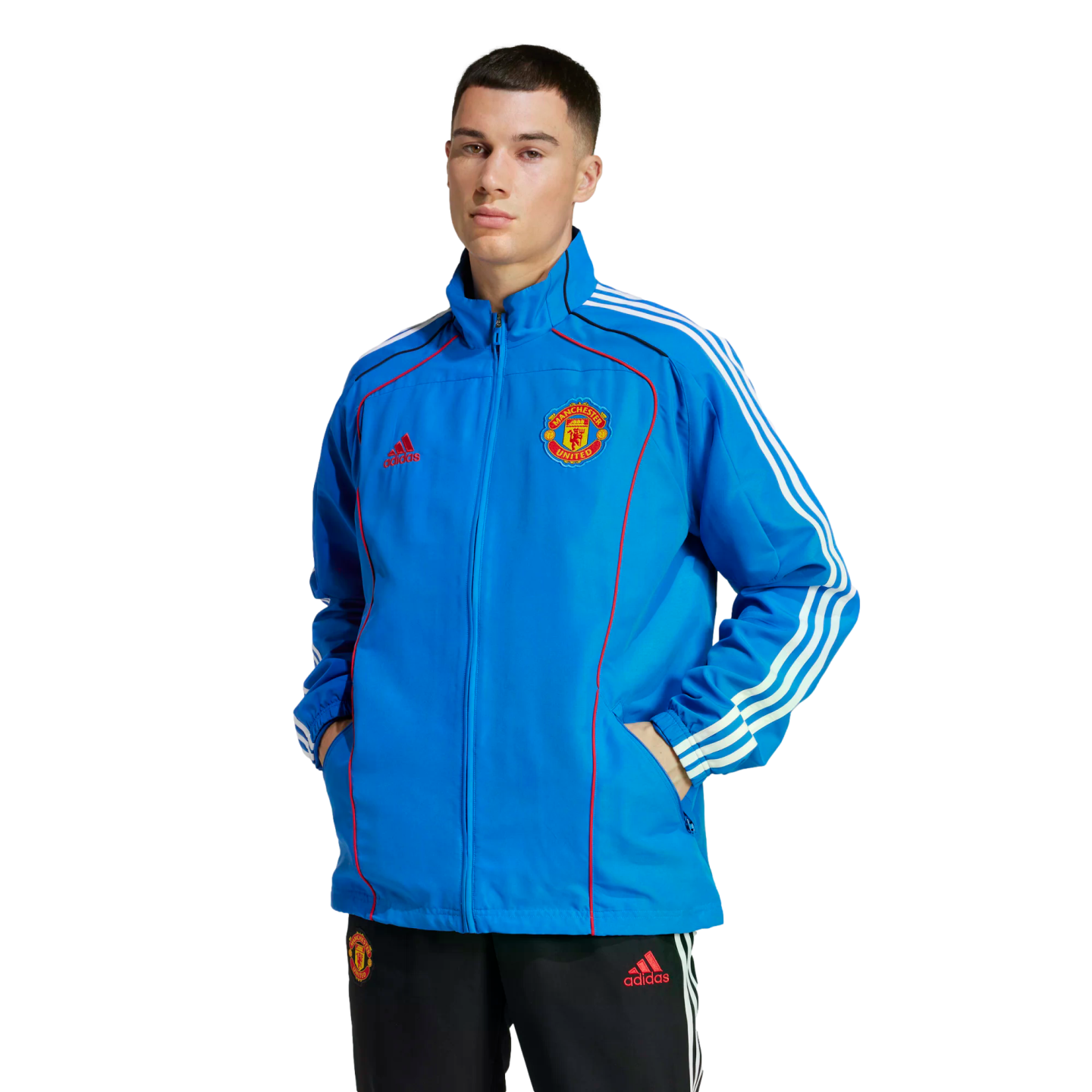 A man models a blue Adidas Manchester United track jacket and black track pants against a plain white background. The jacket features white stripes and red accents.