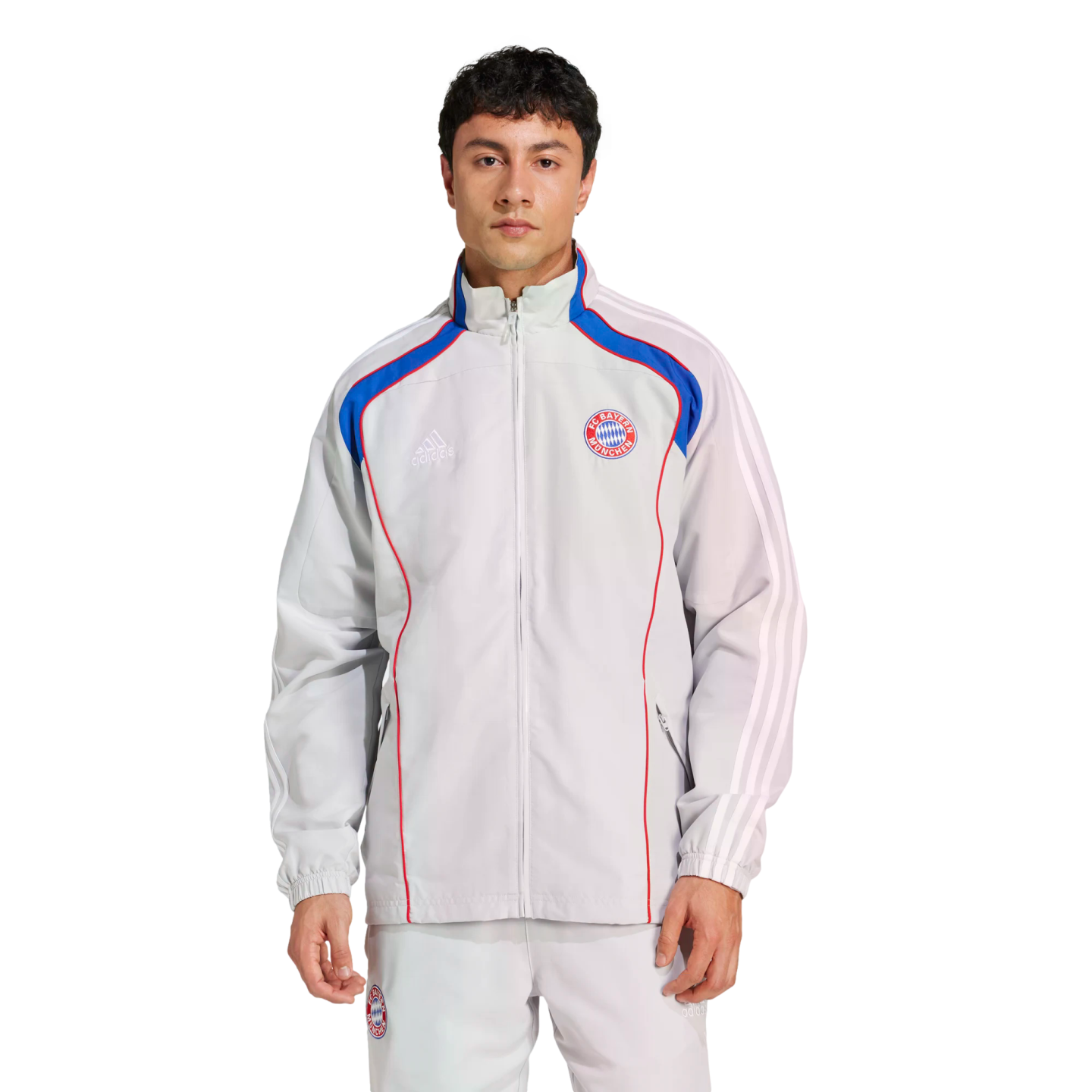 Man wearing a light gray Adidas FC Bayern Munich tracksuit with blue and red accents against a white background.