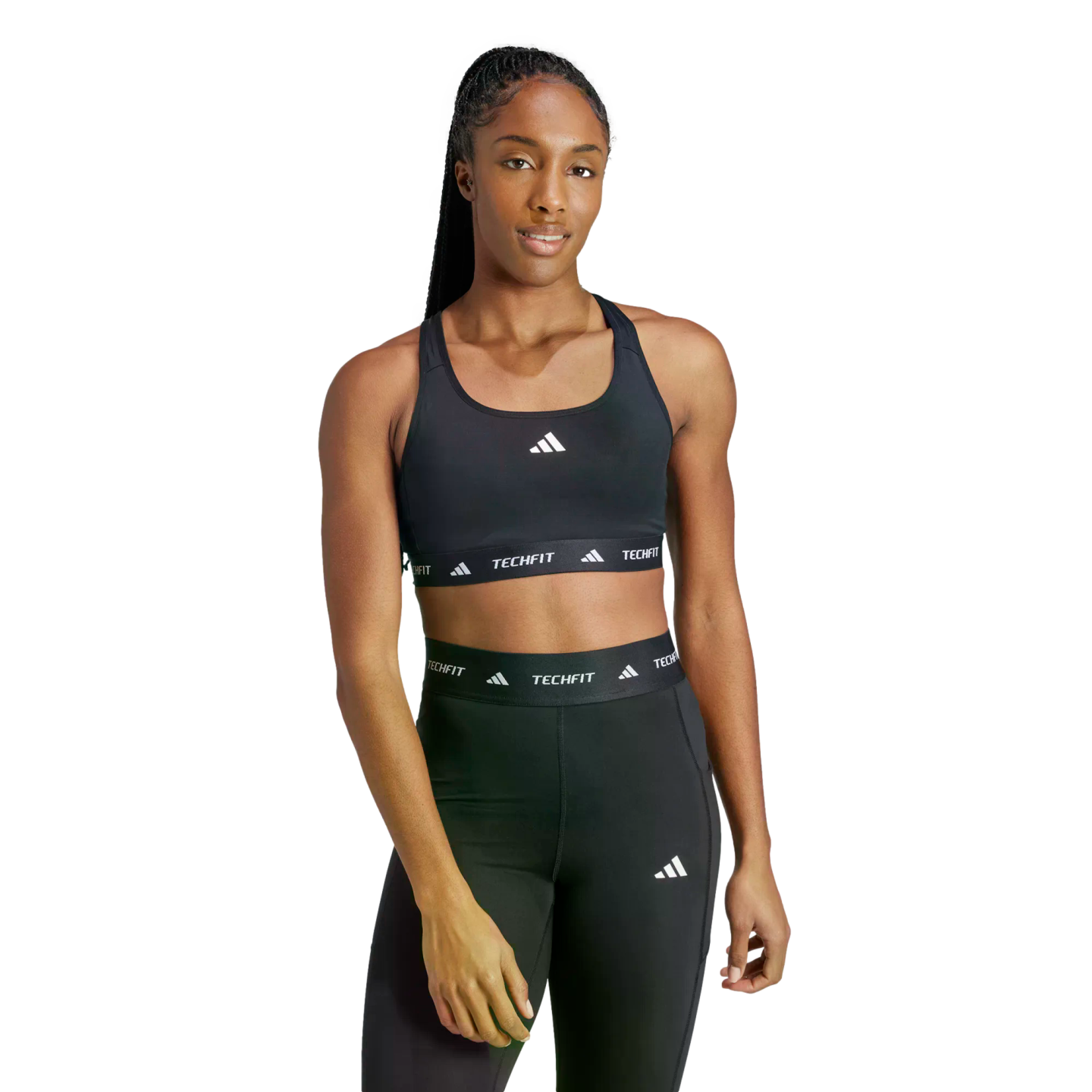 A woman wearing a black Adidas TECHFIT sports bra and matching leggings against a black background.