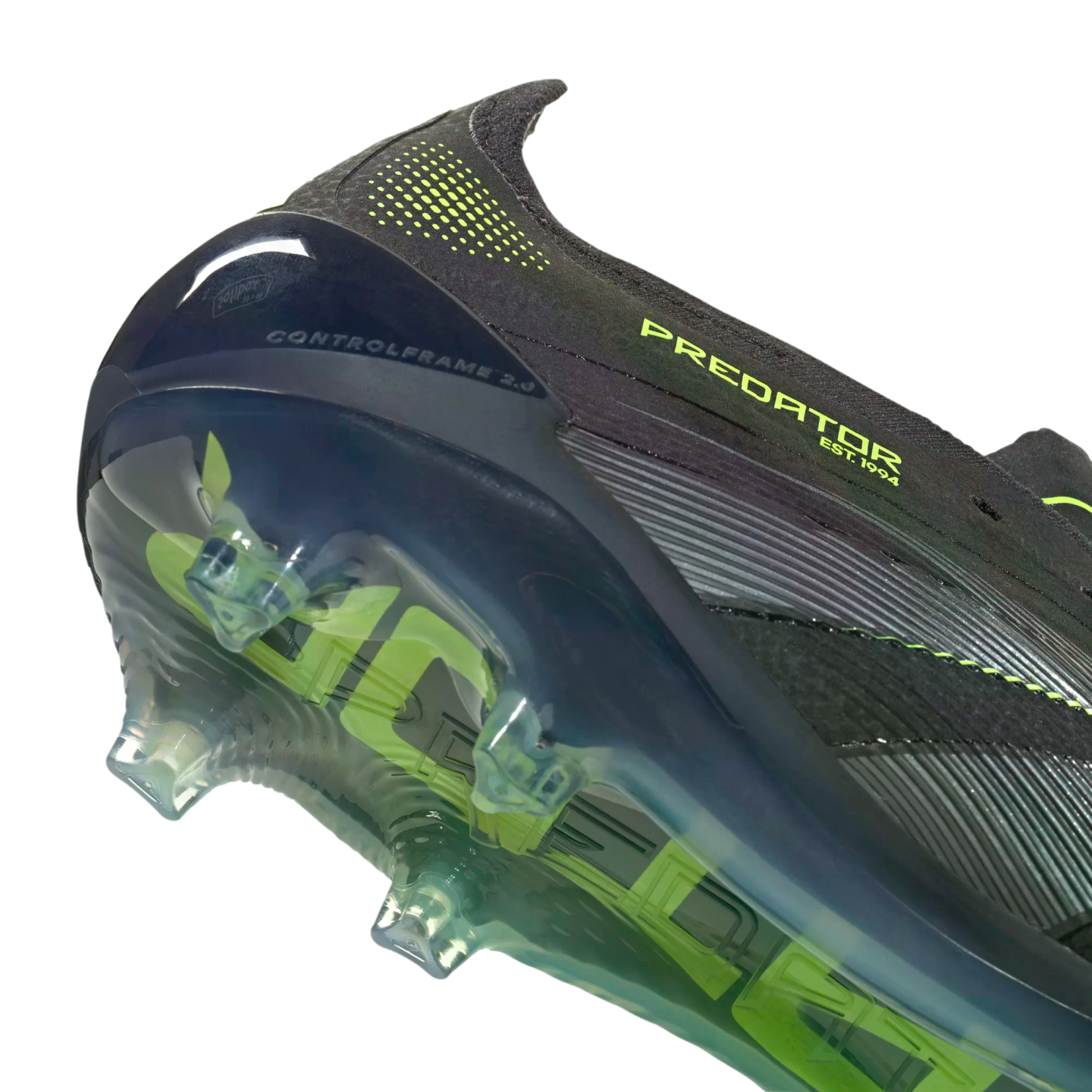 Close-up of a black Predator soccer cleat's heel and soleplate, featuring lime green accents and a translucent control frame with studs against a black background.