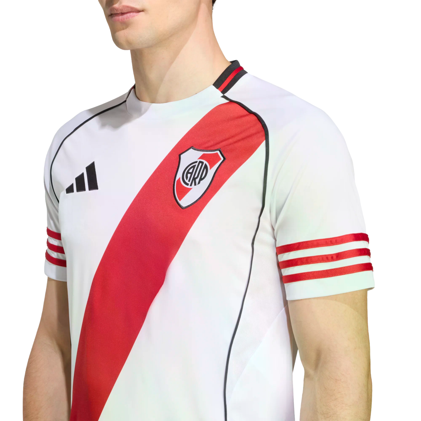 A person wears a white River Plate football jersey featuring a red diagonal sash, three red stripes on the sleeves, and the Adidas logo. Set against a plain white background.
