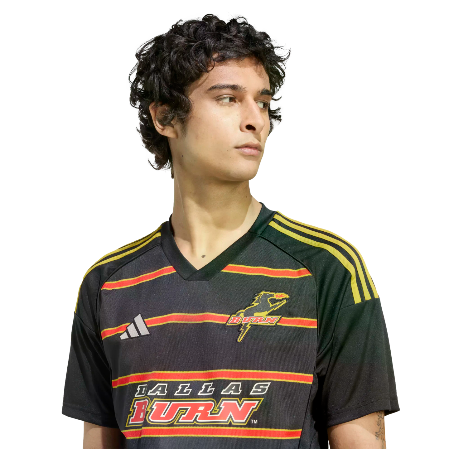 A young man with dark curly hair wearing a black Adidas Dallas Burn soccer jersey with red and yellow horizontal stripes, looking to the side.