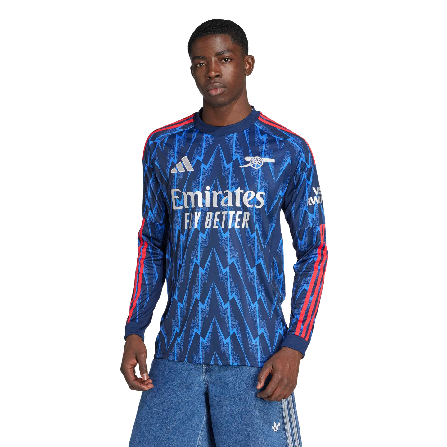 A man models a blue long-sleeved Arsenal jersey with a light blue zigzag pattern and red shoulder stripes, set against a black background.