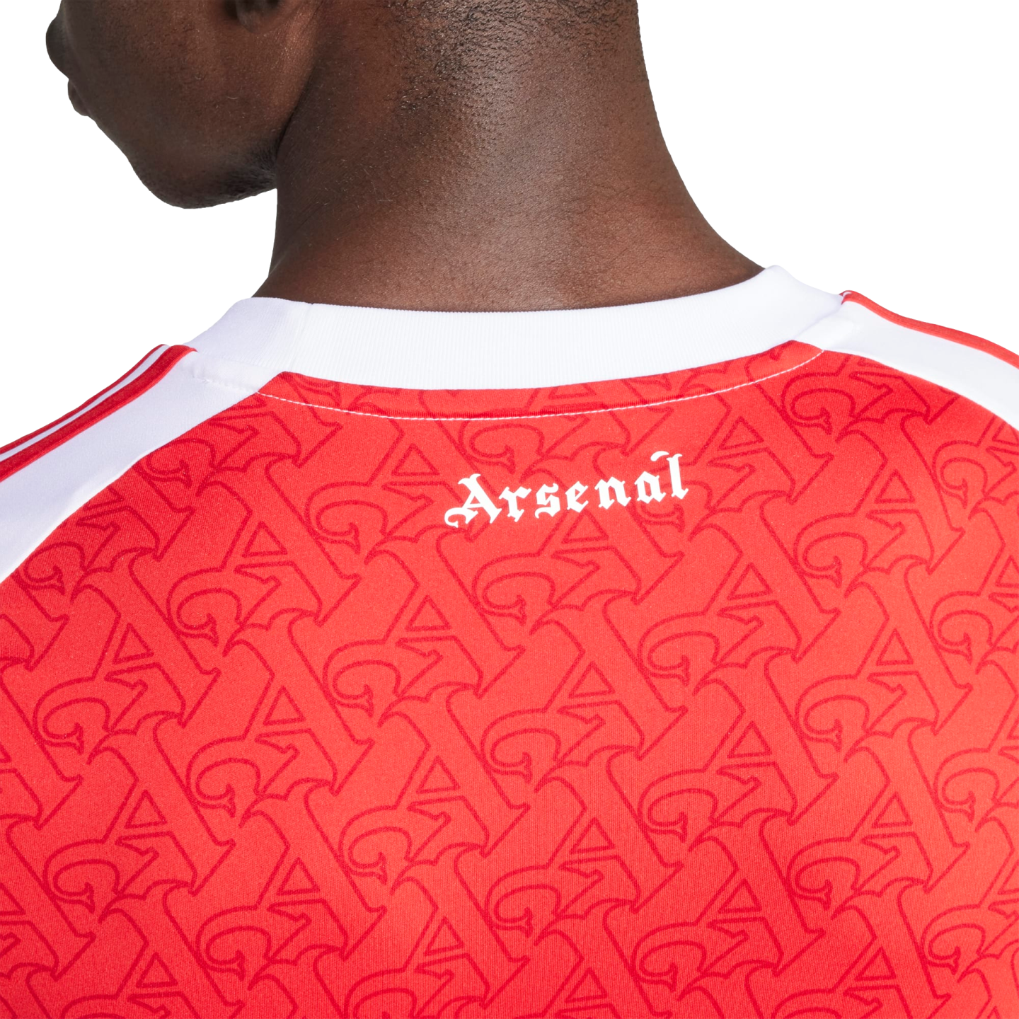A close-up of the back of a red Arsenal jersey with a white collar, featuring a repeating "A" pattern and "Arsenal" printed in white gothic font below the neckline.