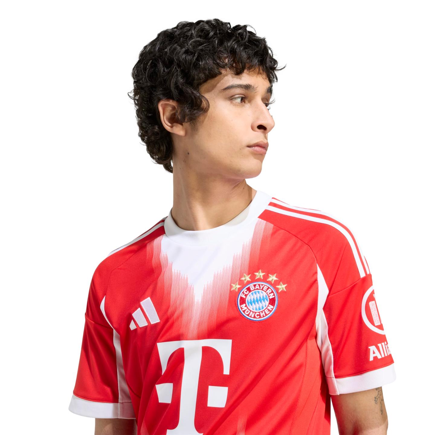 A young man with dark curly hair wears a red and white FC Bayern Munich soccer jersey. He looks off-camera against a plain white background.