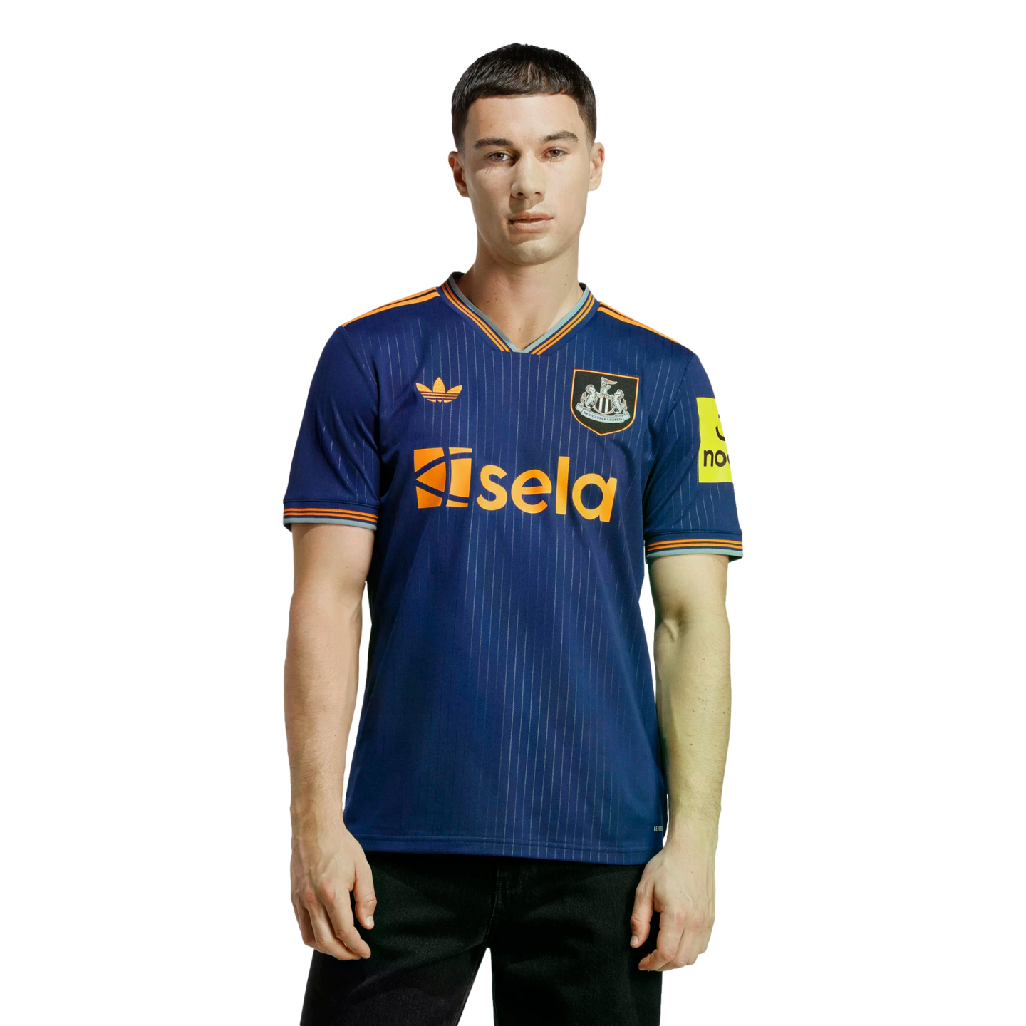 A man models a navy blue Newcastle United soccer jersey with orange trim, featuring thin vertical stripes, the Sela sponsor logo, and Adidas trefoil logo, against a black background.