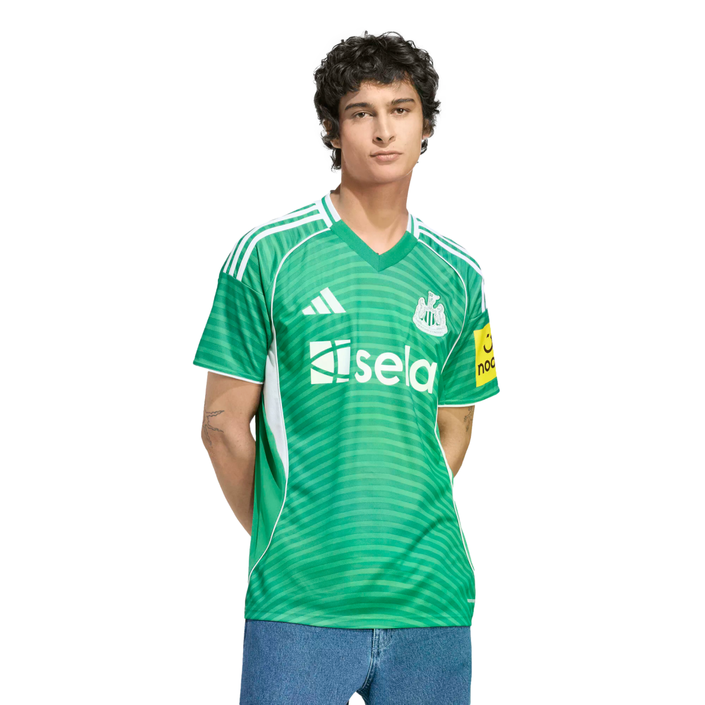 A man wearing a green Newcastle United football jersey with white details and a "sela" sponsor logo, paired with blue jeans against a black background.