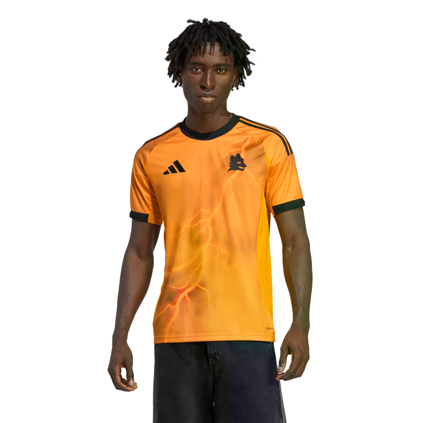 A young man wearing a bright orange Adidas jersey with a lightning bolt graphic and wolf crest, standing against a solid black background.