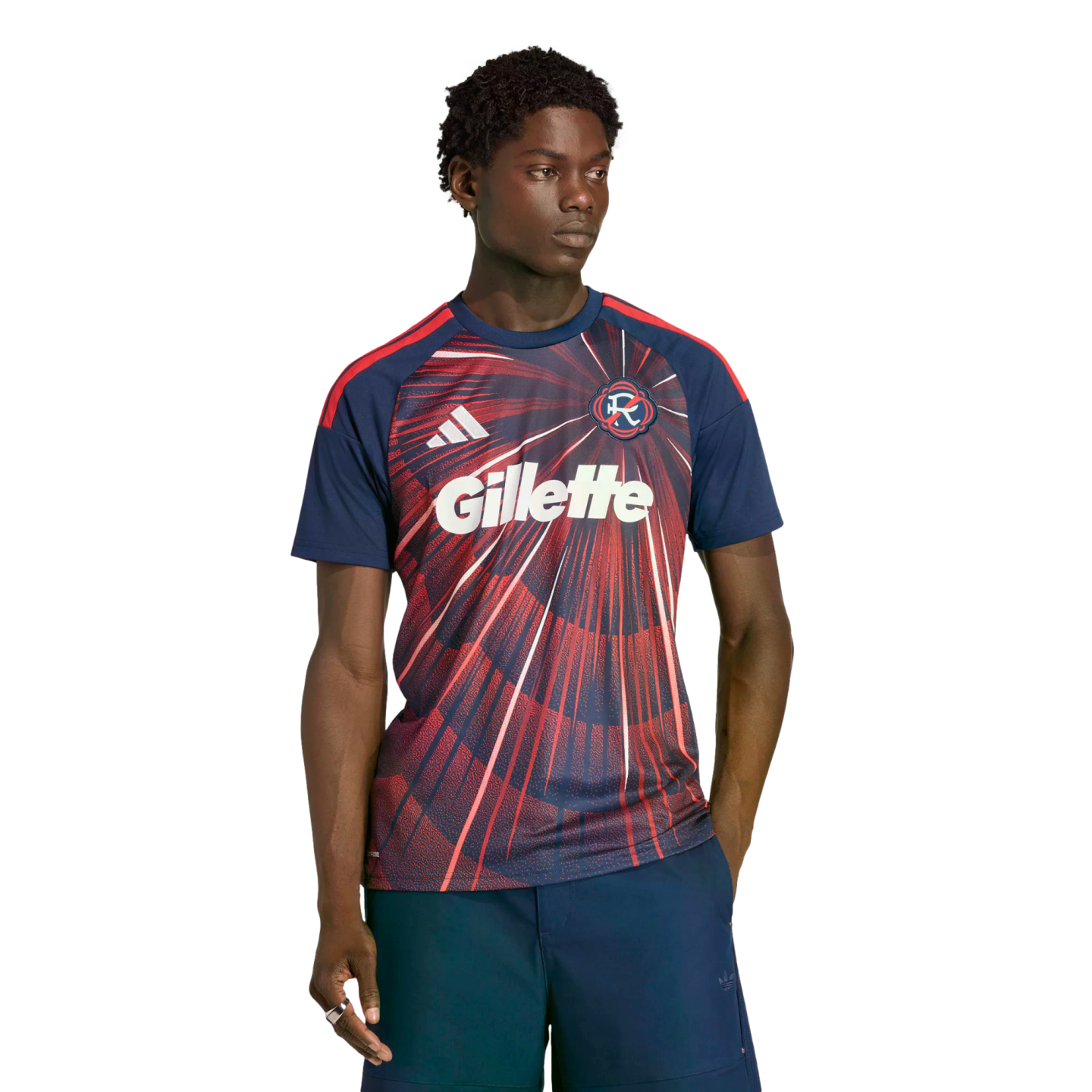 A man wearing a navy and red Adidas soccer jersey with a large white Gillette logo and dark shorts, posed against a black background.