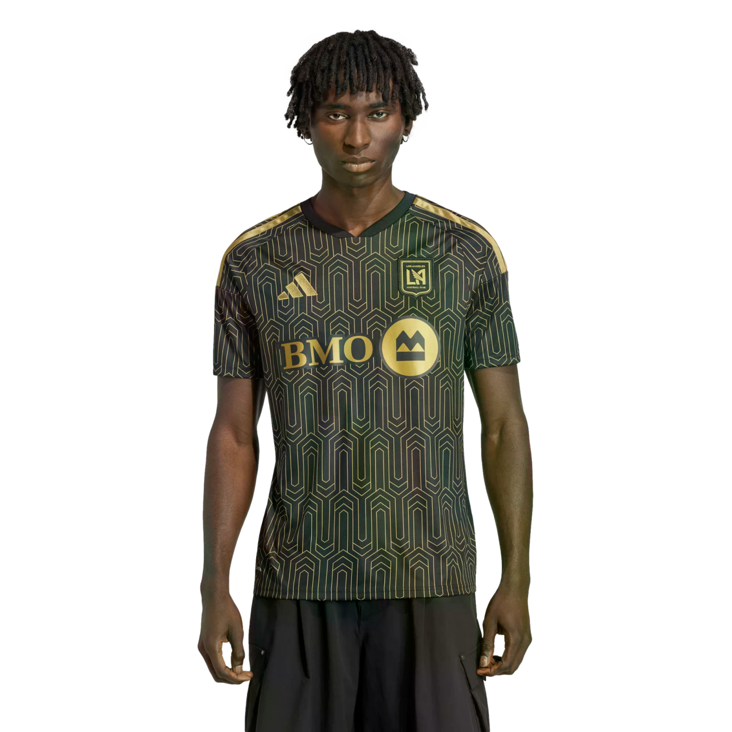 A man with dreadlocks wears a black and gold LAFC soccer jersey with a geometric pattern against a solid black background.