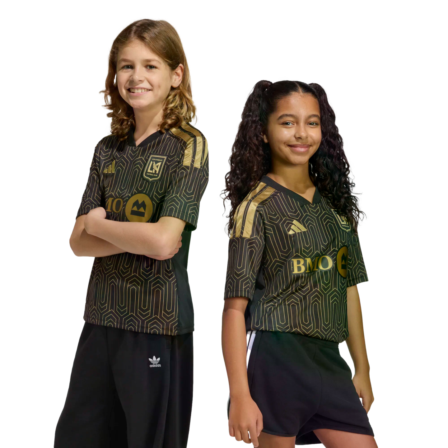 Two smiling children pose in matching black and gold Los Angeles FC soccer jerseys against a solid black background. One wears black pants, and the other wears black shorts.