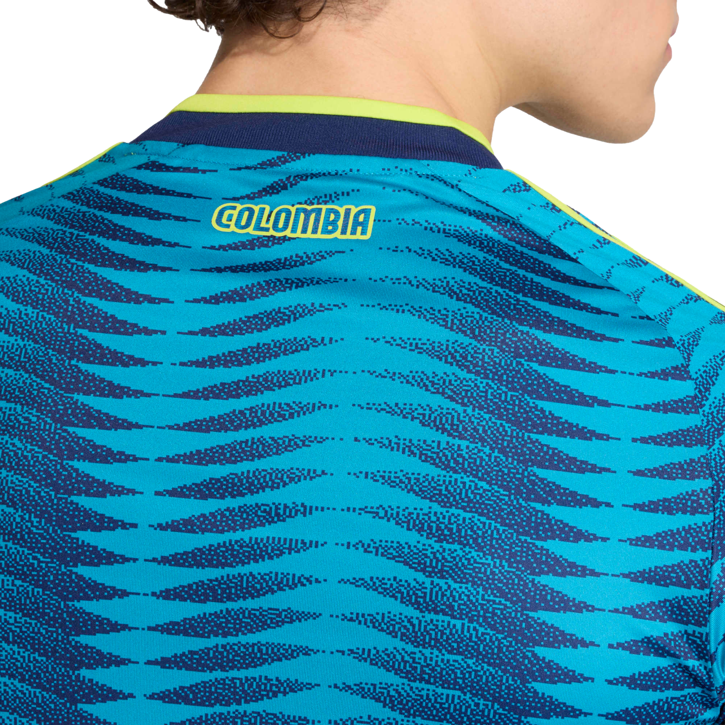 Close-up of the back of a teal and blue patterned soccer jersey with "COLOMBIA" in yellow text near the lime green and navy collar.