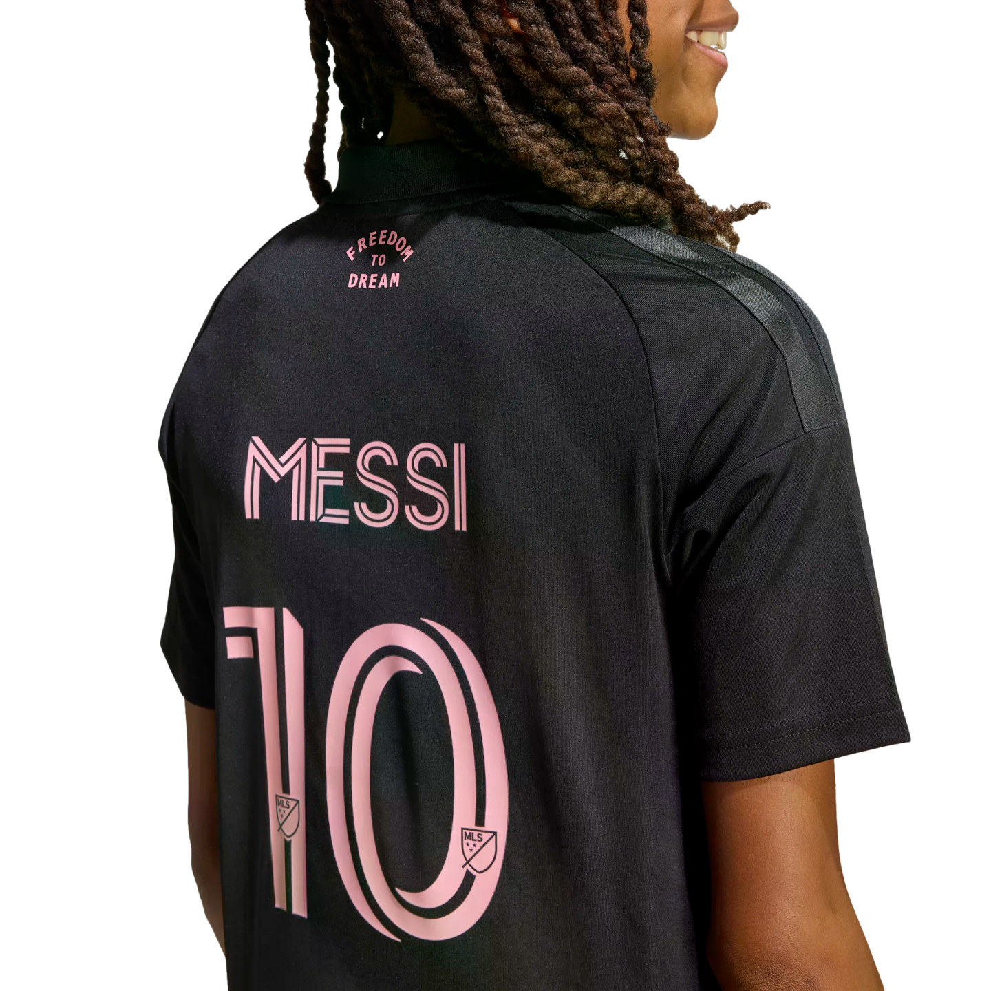 Back view of a person with long braids wearing a black Inter Miami jersey with pink lettering for "FREEDOM TO DREAM", "MESSI", and the number 10 on a black background.