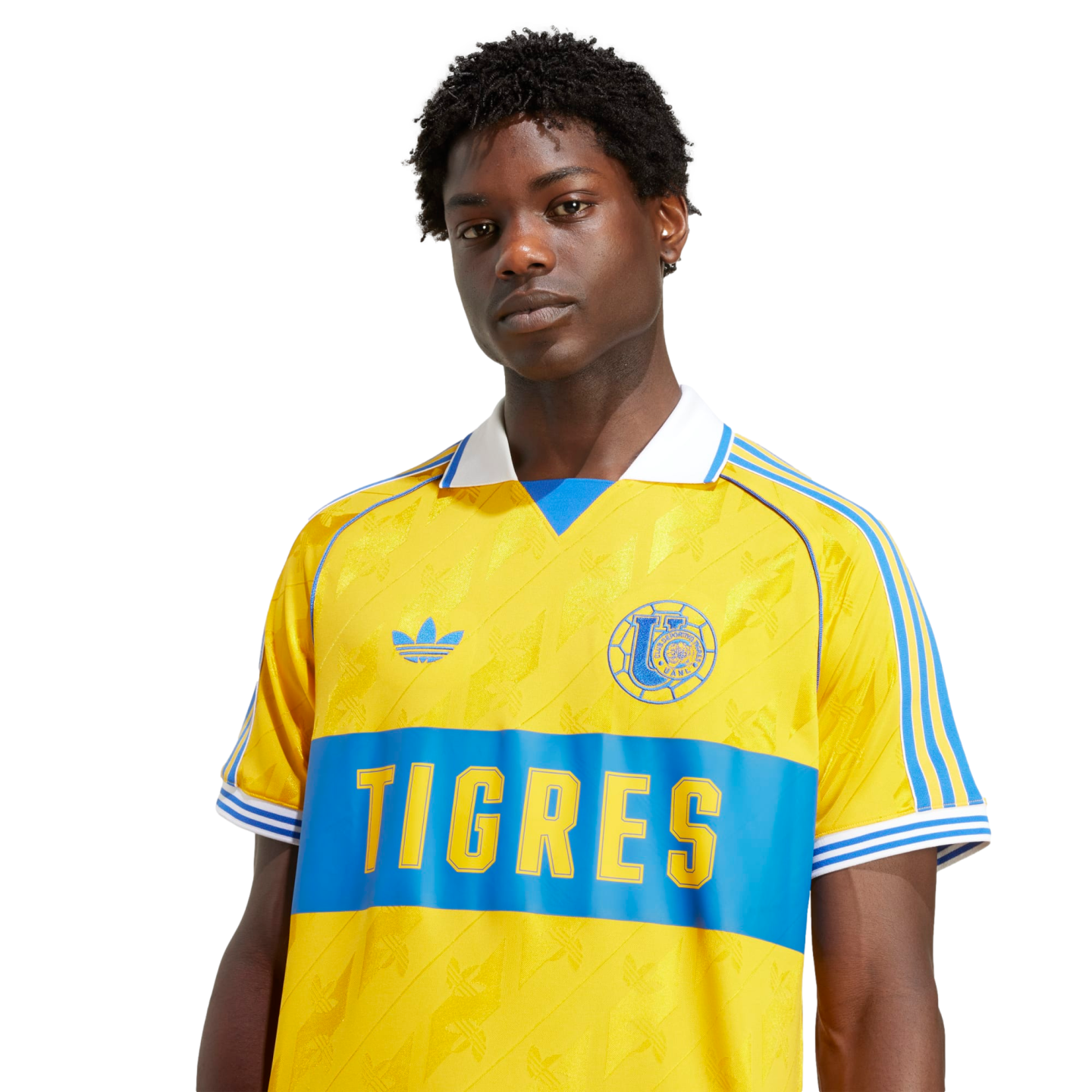 A man wearing a yellow and blue Adidas Tigres UANL soccer jersey with a white collar against a black background.