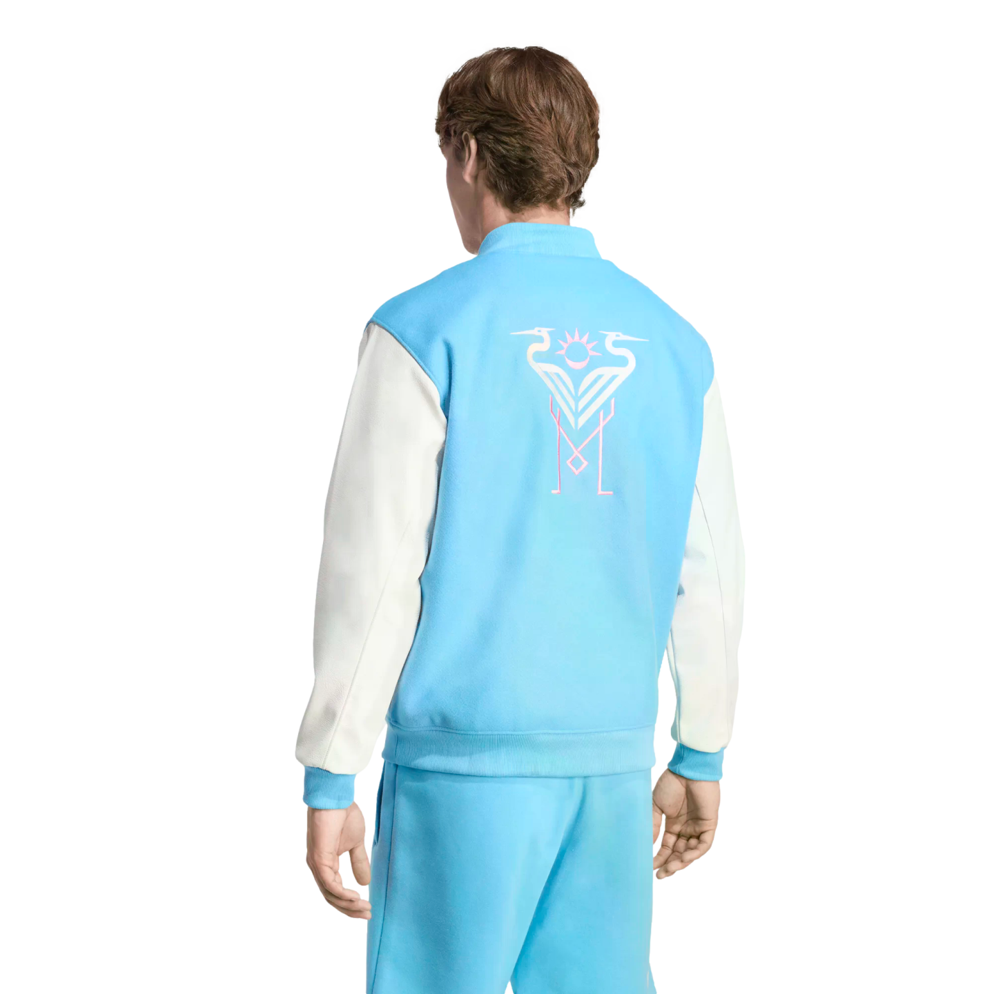 Back view of a man wearing a light blue and white varsity jacket with a stylized bird graphic on the back and matching light blue pants.