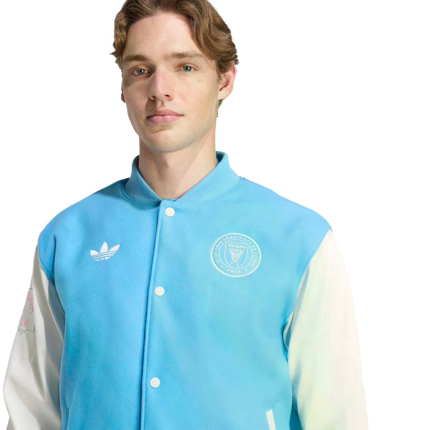 A man with light brown hair wearing a light blue and white Adidas varsity jacket featuring the Inter Miami CF crest.